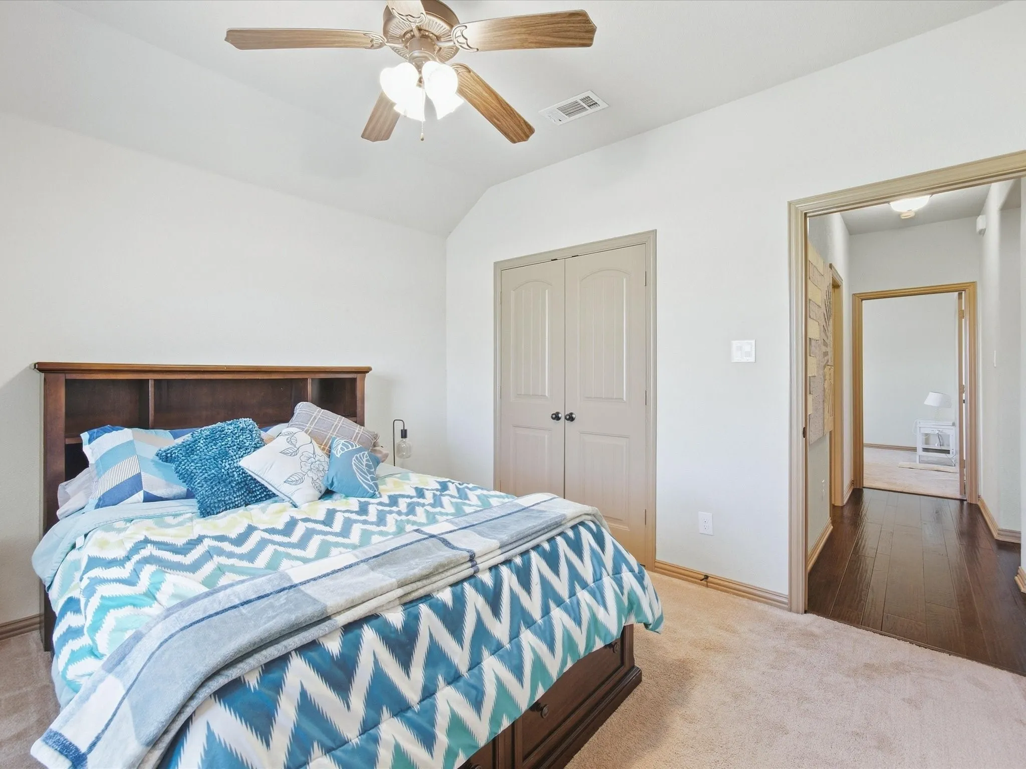 Vaulted ceiling with a ceiling fan, light-colored carpeting, built-in shelving, wood-finish flooring in the hallway, and paneled closet doors