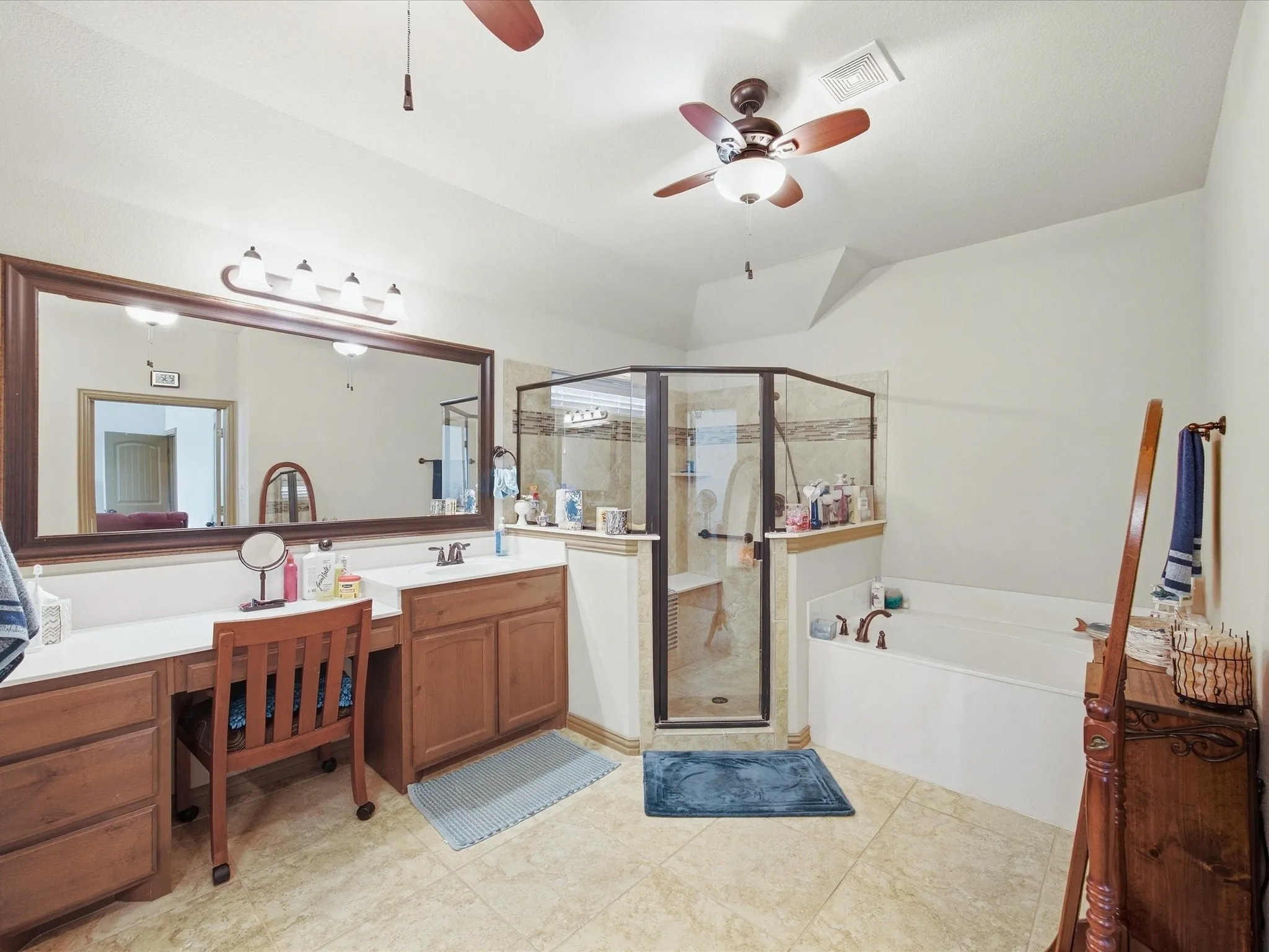 Expansive bathroom featuring a dual vanity with wood cabinetry, a built-in makeup vanity, a glass-enclosed shower, a separate soaking tub, and tile flooring
