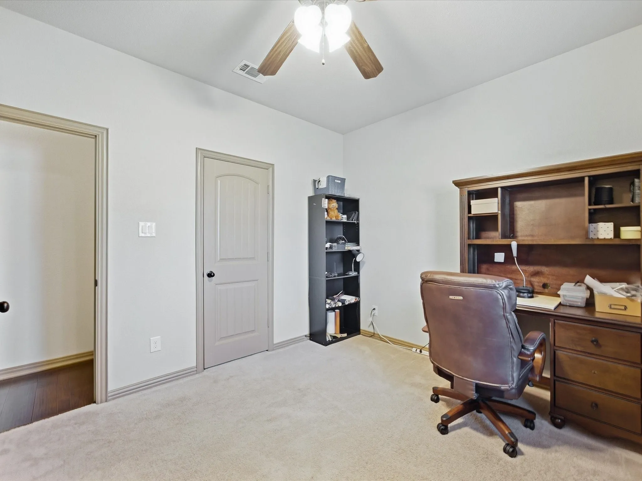 Soft carpet flooring, light-toned walls, and wood-finish ceiling fan