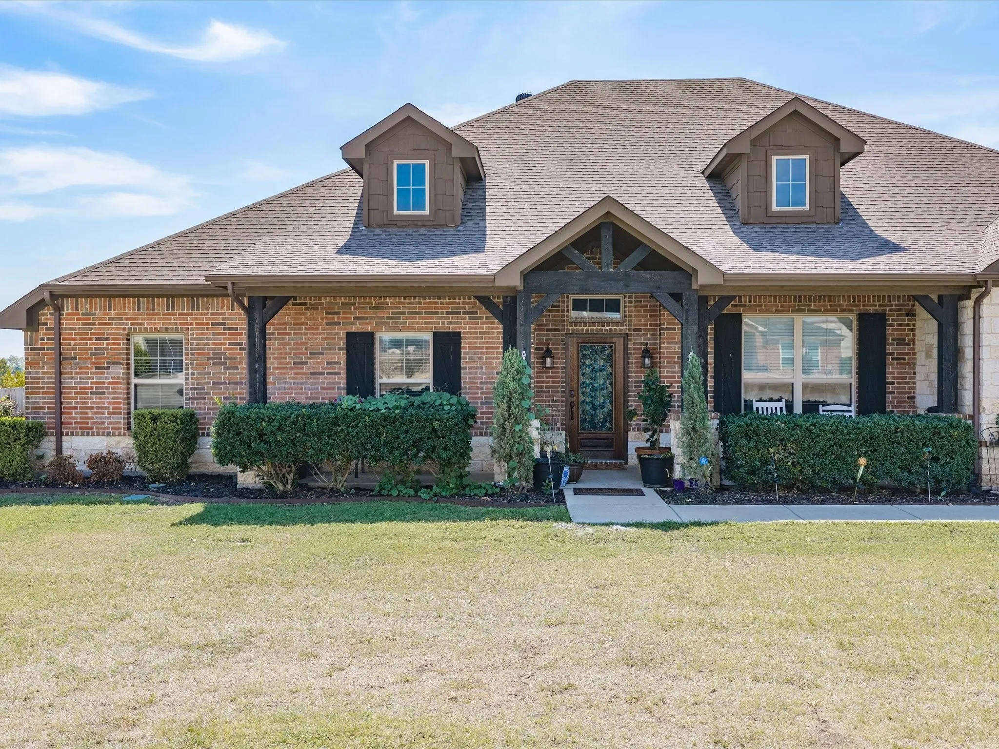 Brick exterior with dormer windows, covered entry, and dark wood-finish columns