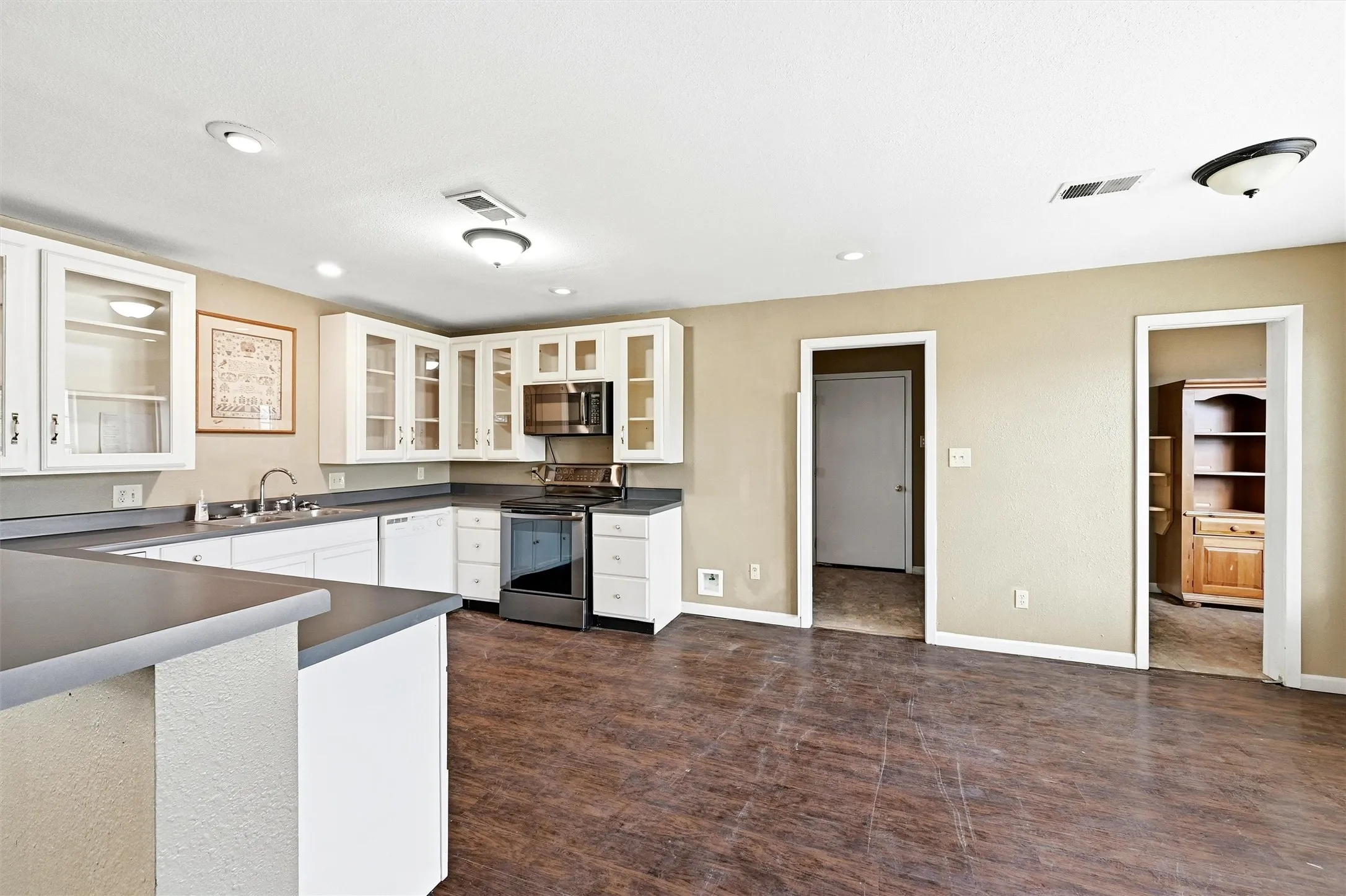 Kitchen featuring dark countertops, appliances with stainless steel finishes, glass insert cabinets, white cabinets, and recessed lighting