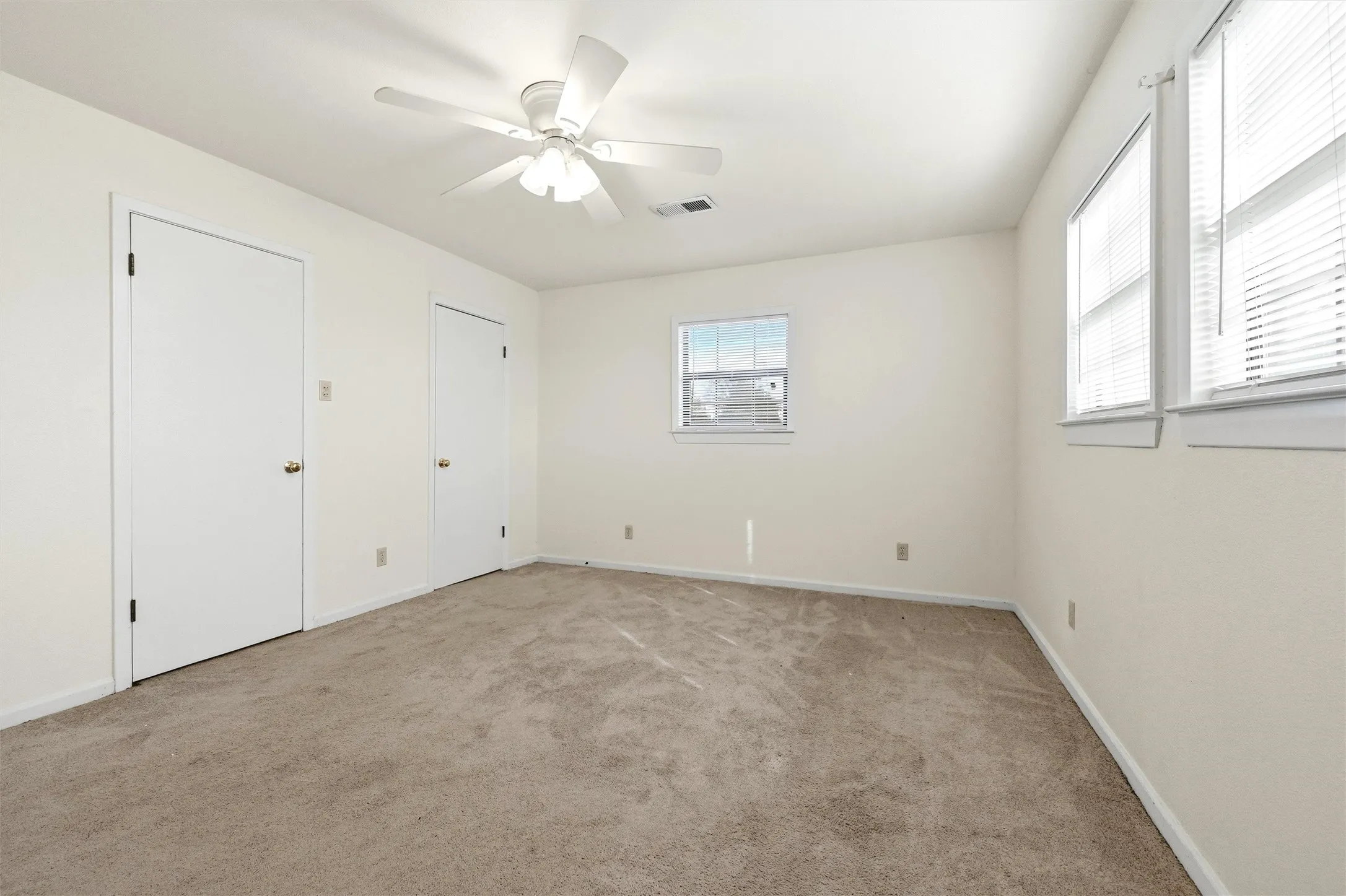 Unfurnished bedroom with light colored carpet, ceiling fan, and multiple closets