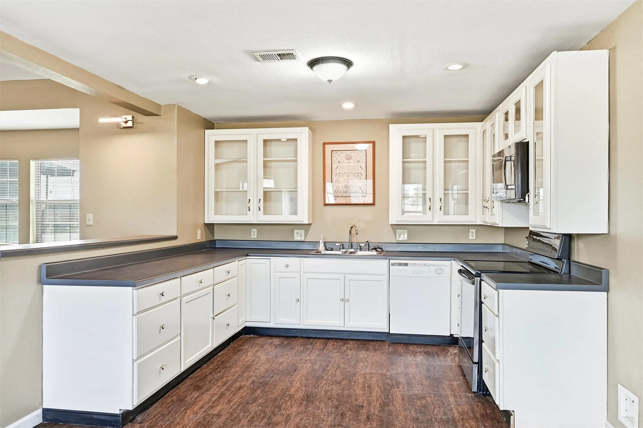 Kitchen featuring dark countertops, electric range, glass insert cabinets, white cabinets, and dishwasher