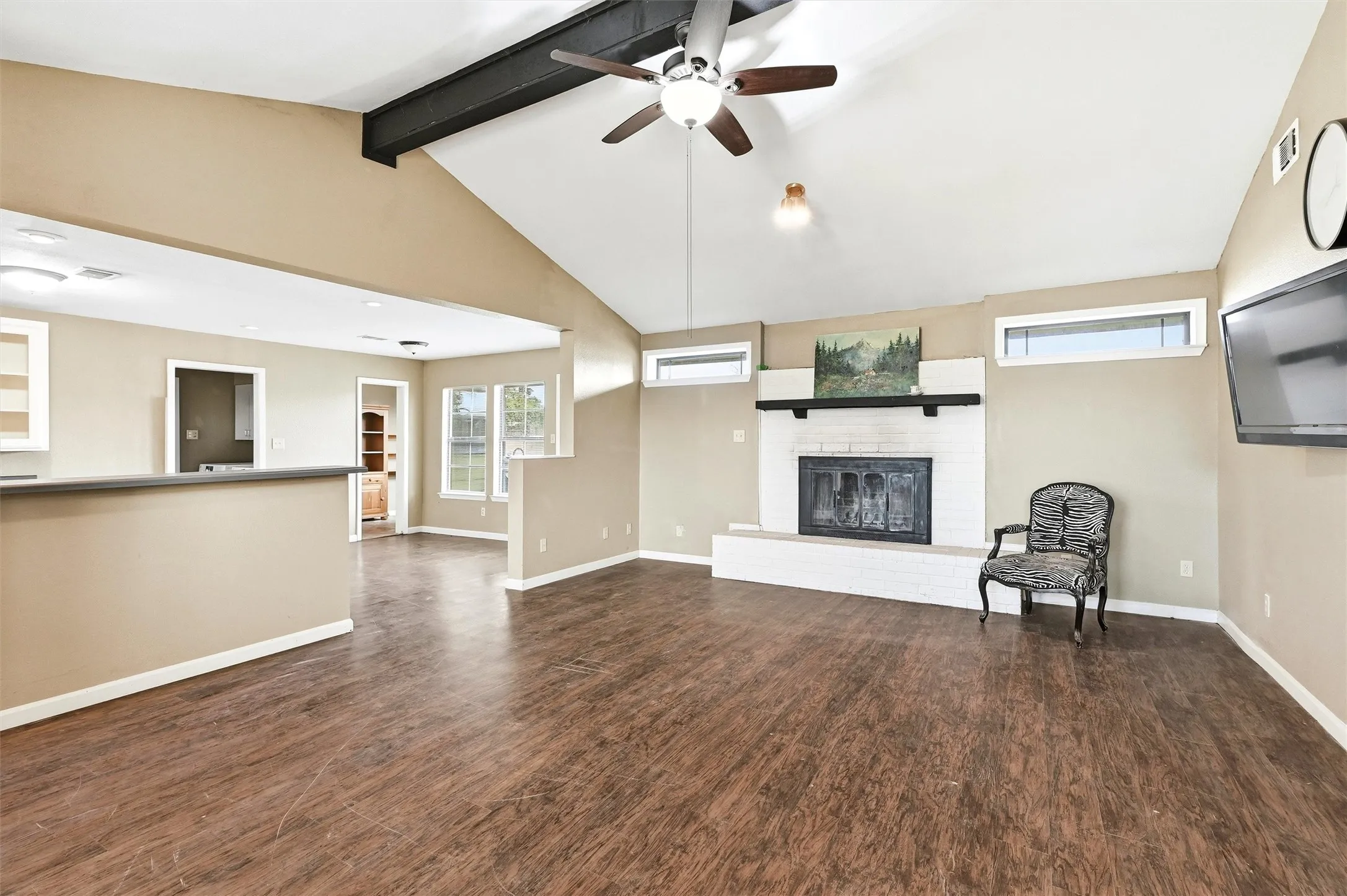 Unfurnished living room featuring beam ceiling, ceiling fan, a brick fireplace, dark wood-type flooring, and high vaulted ceiling