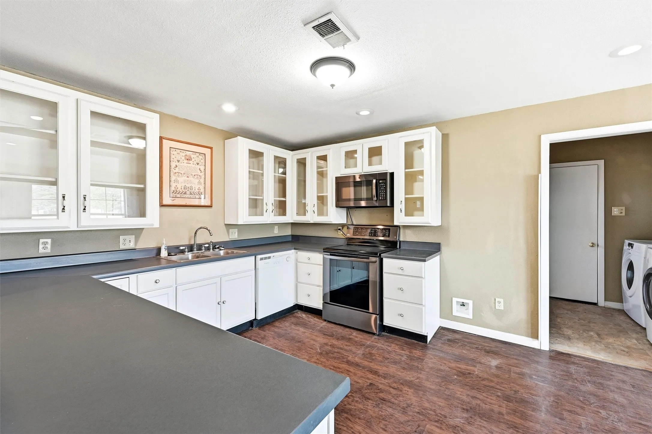 Kitchen featuring appliances with stainless steel finishes, dark countertops, white cabinets, glass insert cabinets, and dark wood-type flooring