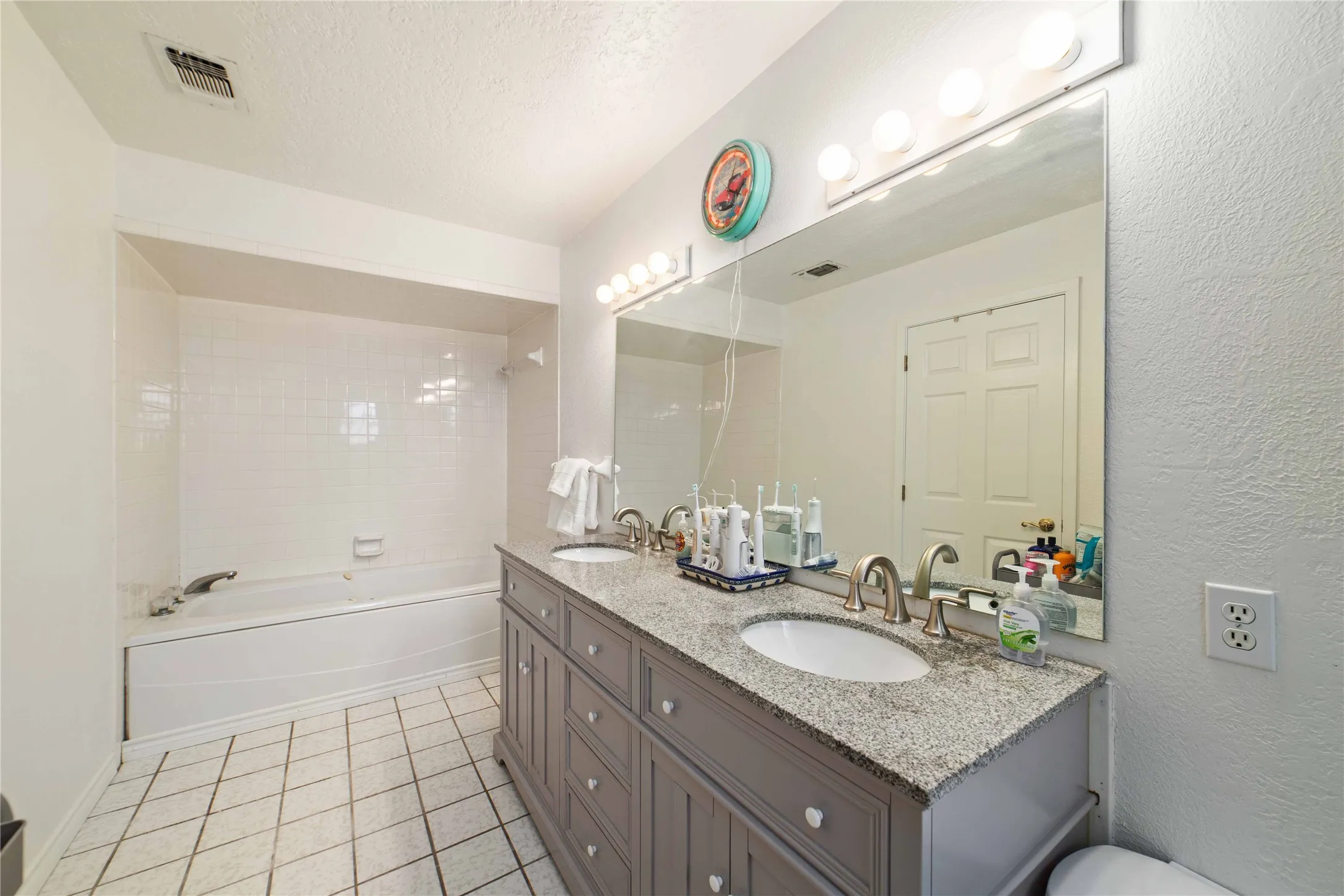 Bathroom with a textured wall, visible vents, tile patterned flooring, and a sink