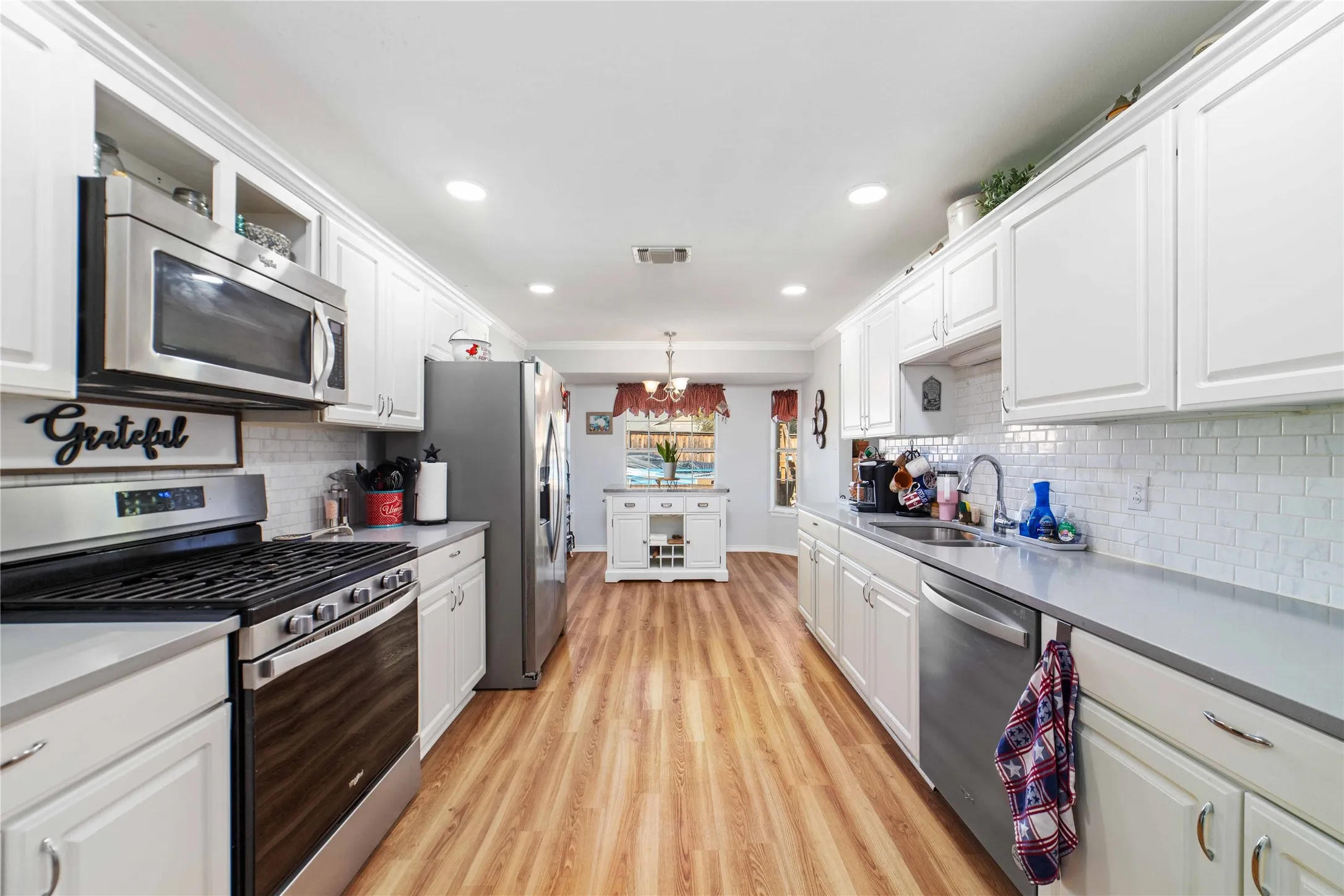 Kitchen with white cabinets, appliances with stainless steel finishes, a sink, and visible vents
