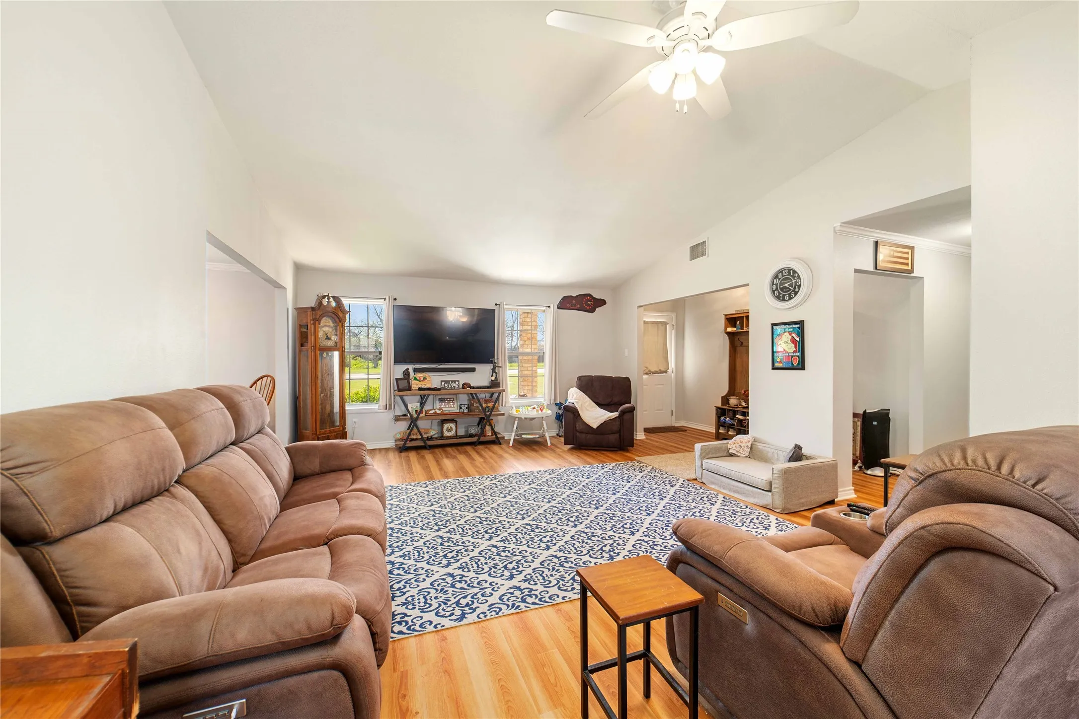 Living room featuring vaulted ceiling, visible vents, light wood-style floors, and ceiling fan