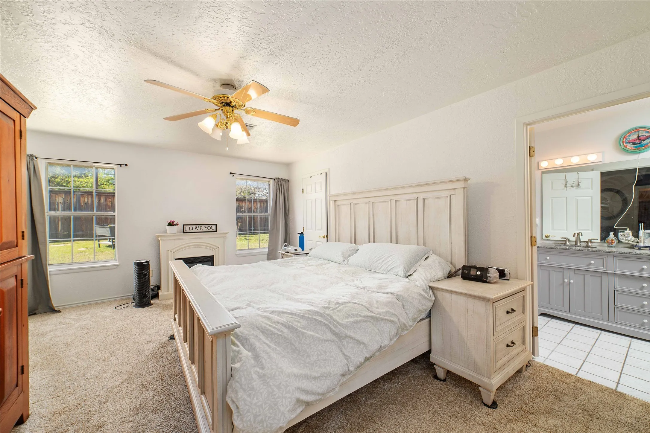 Bedroom with light colored carpet, ensuite bathroom, a textured ceiling, and a fireplace