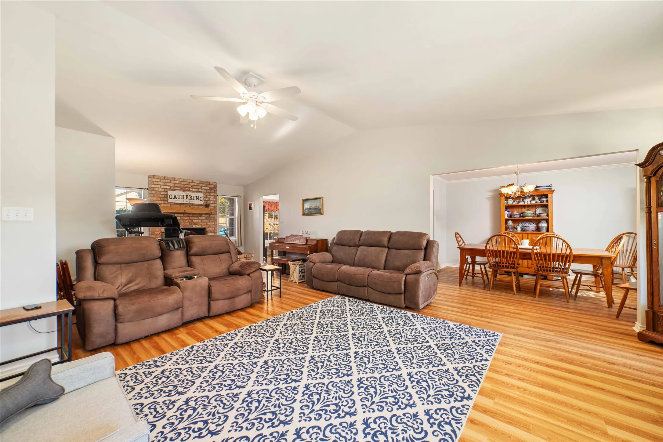 Living room with ceiling fan with notable chandelier, light wood-style flooring, a fireplace, and lofted ceiling