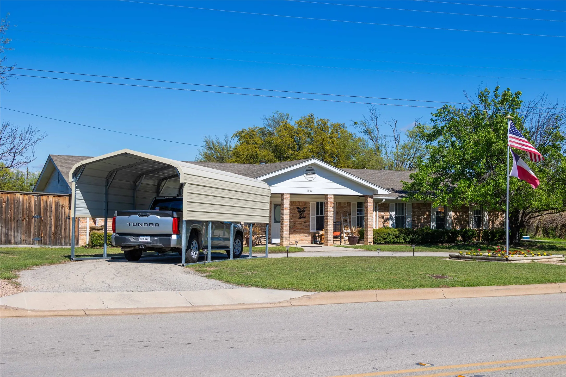 View of front of home with driveway, a carport, fence, a front yard, and brick siding