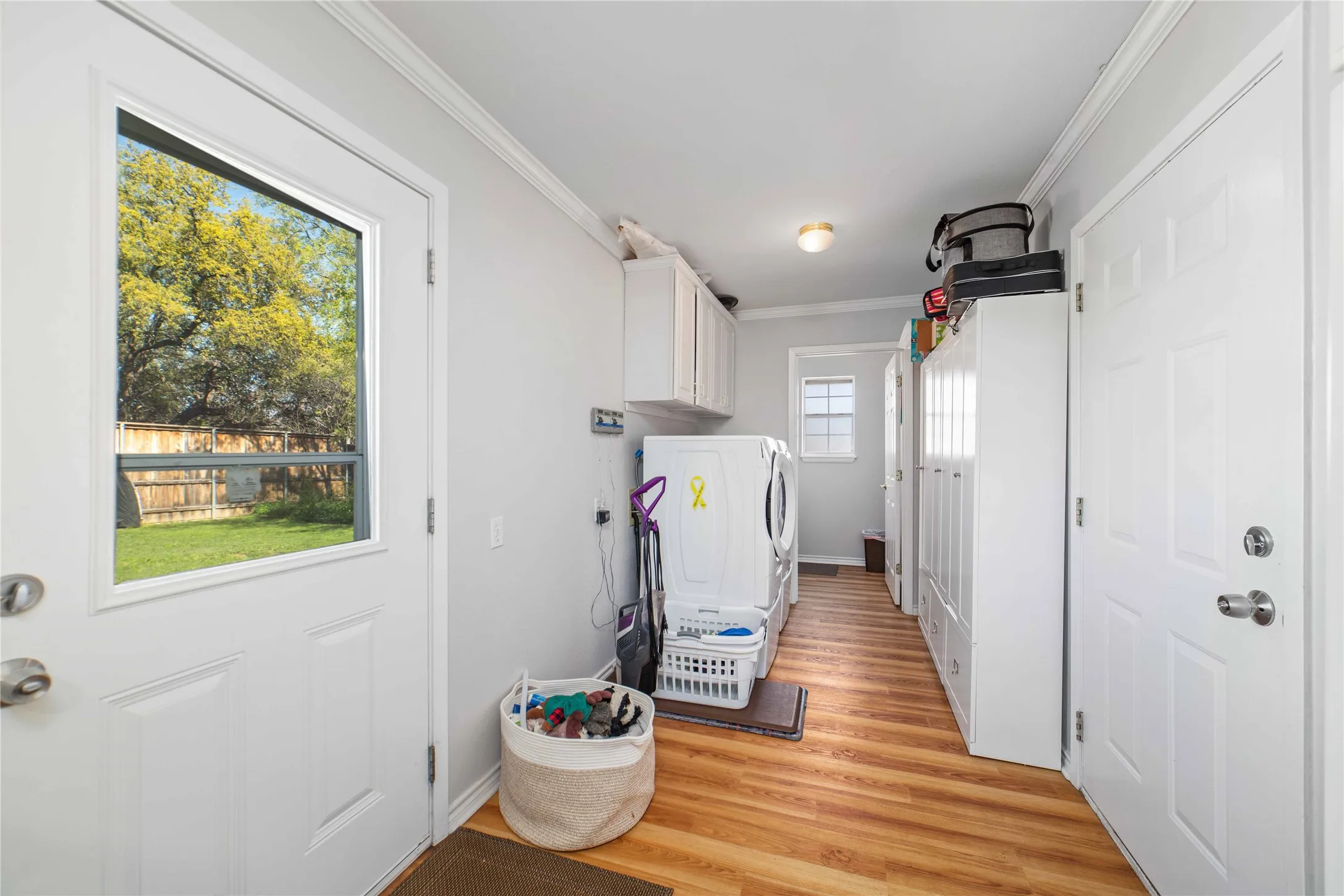Clothes washing area featuring ornamental molding, washing machine and clothes dryer, cabinet space, and light wood finished floors
