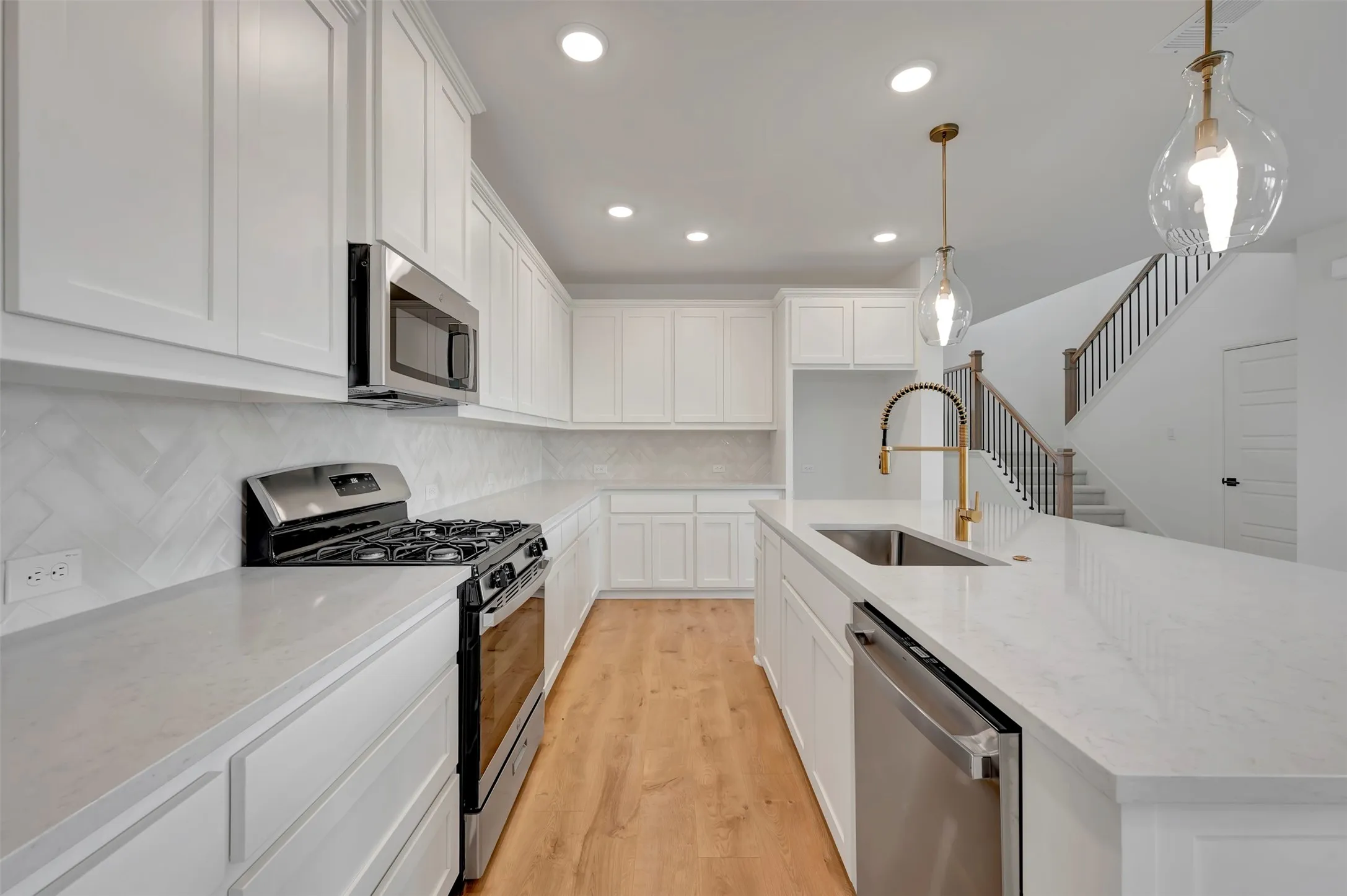 Kitchen with stainless steel appliances, white cabinets, a kitchen island with sink, decorative light fixtures, and light wood-type flooring