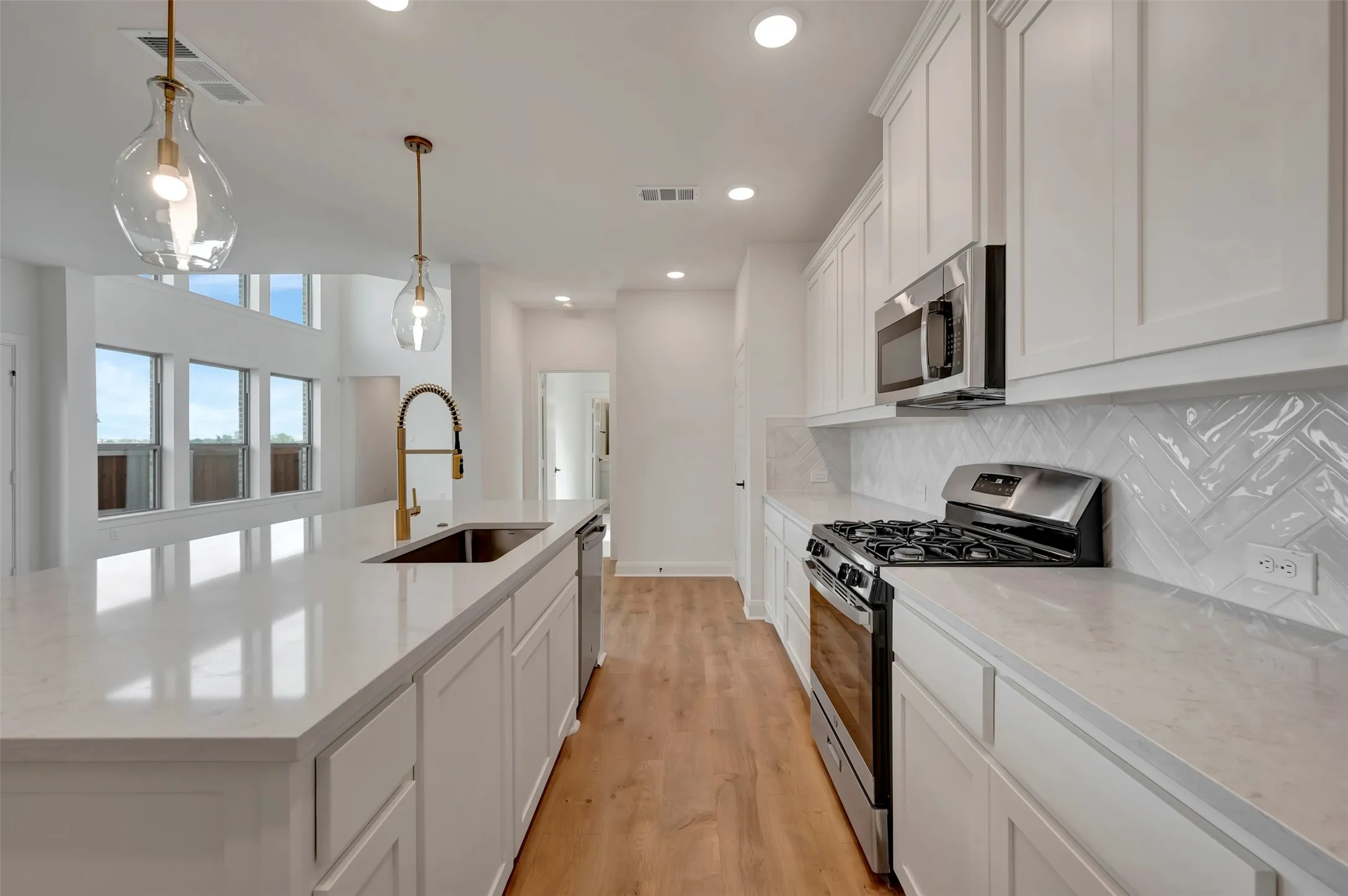 Kitchen featuring stainless steel appliances, white cabinetry, light wood finished floors, a kitchen island with sink, and hanging light fixtures