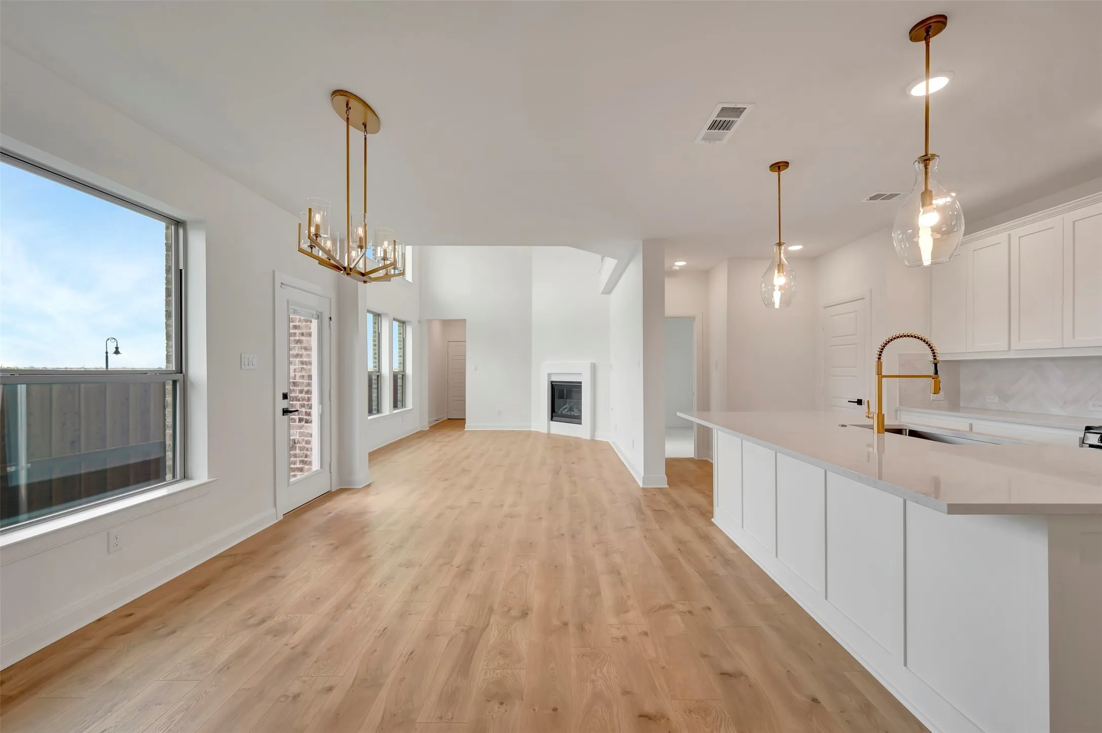 Kitchen with white cabinets, suspended lighting, light wood-type flooring, a fireplace, and a kitchen island with sink