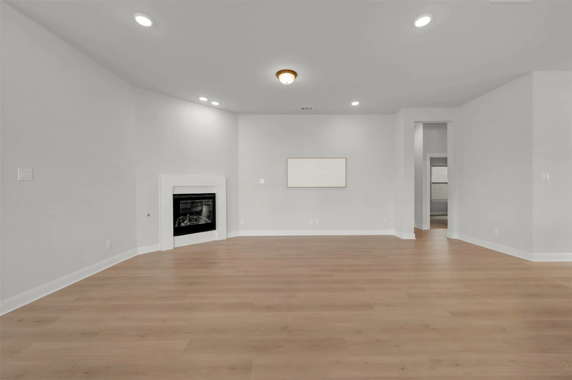 Unfurnished living room featuring a glass covered fireplace, light wood-style flooring, and recessed lighting