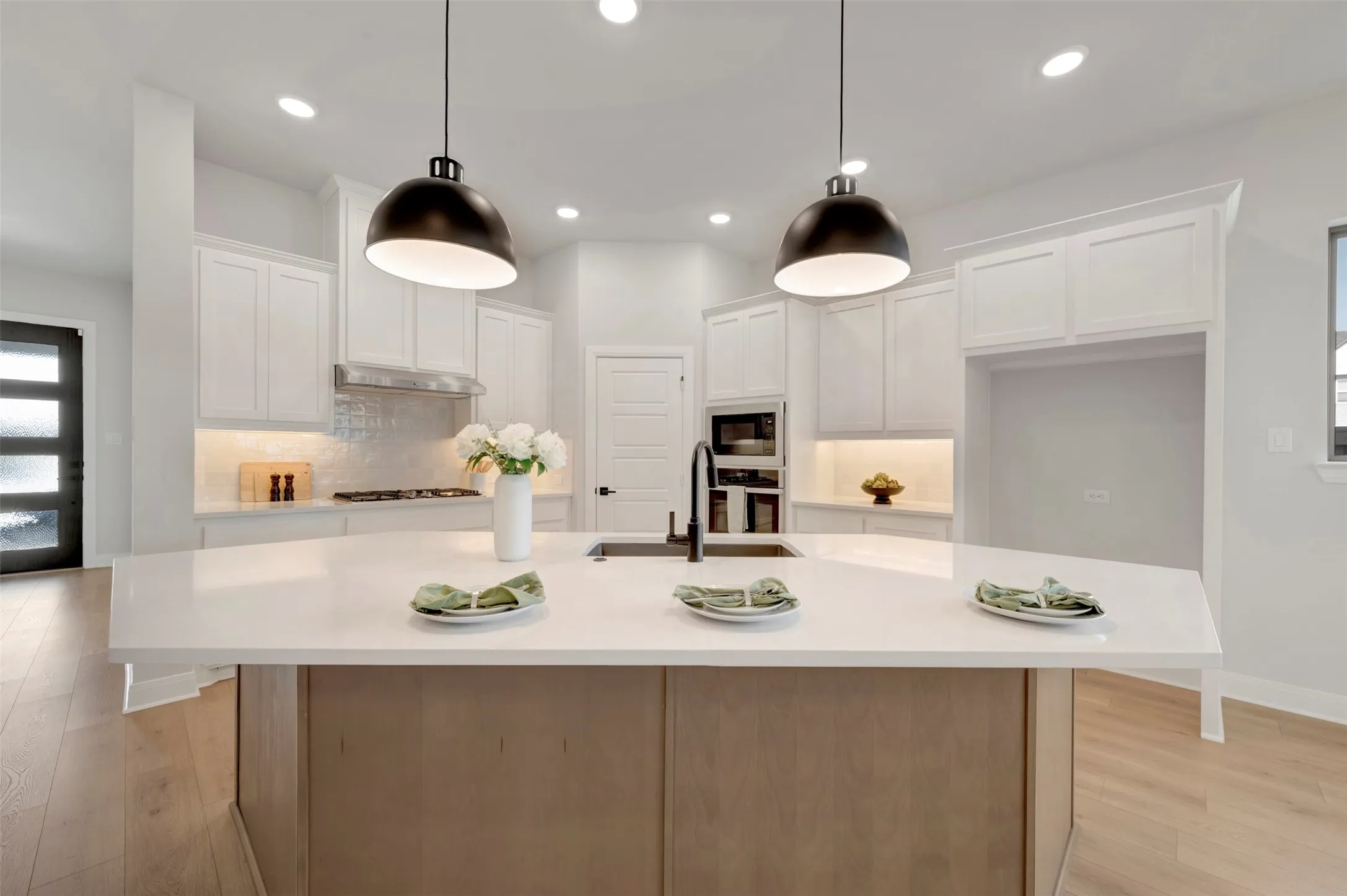 Two tone kitchen featuring light wood-style floors, a kitchen island with sink, oven, decorative backsplash, and two tone cabinets