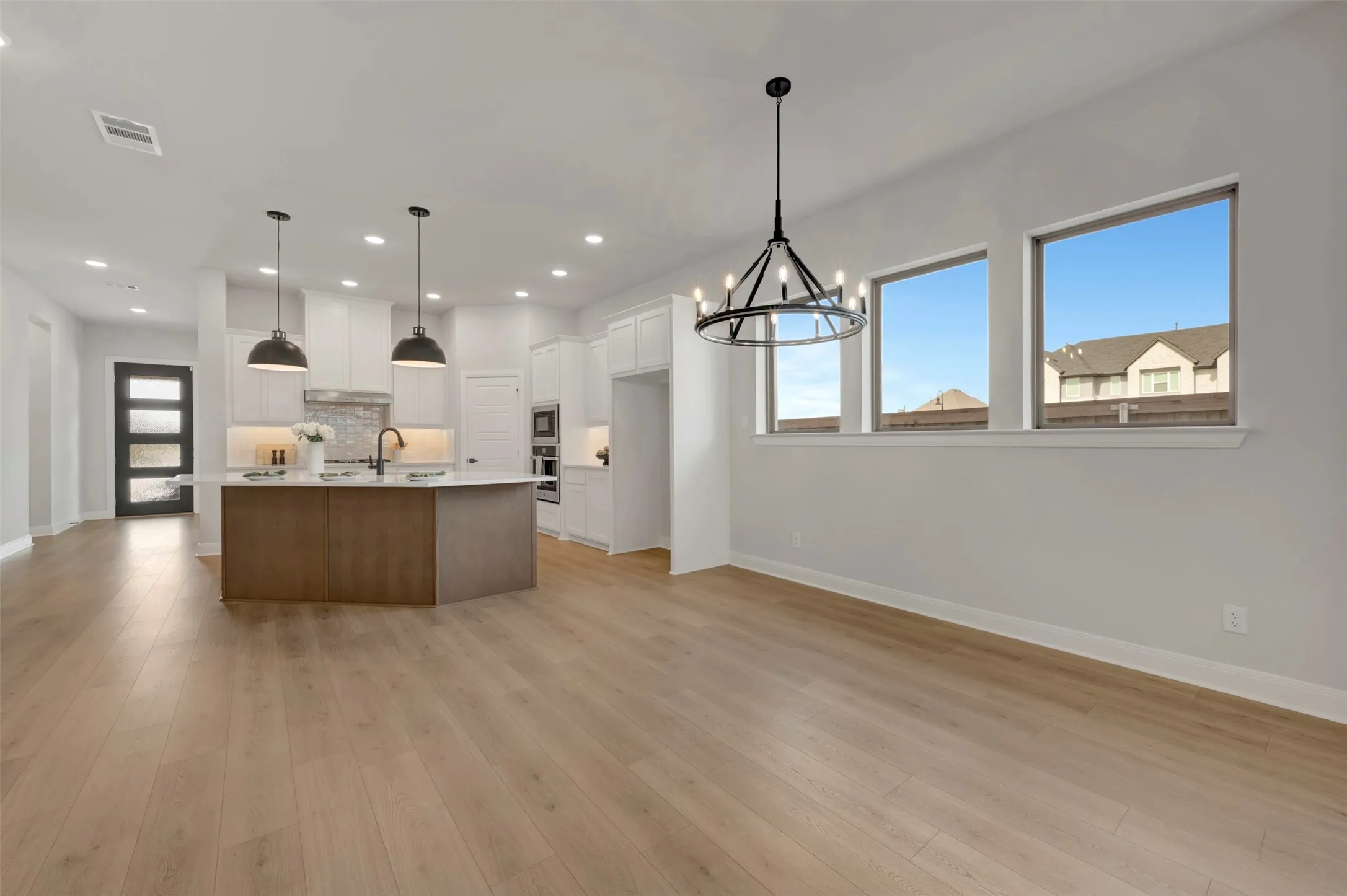 Kitchen with a large island, open floor plan, suspended lighting, two tone cabinets, and light wood finished floors