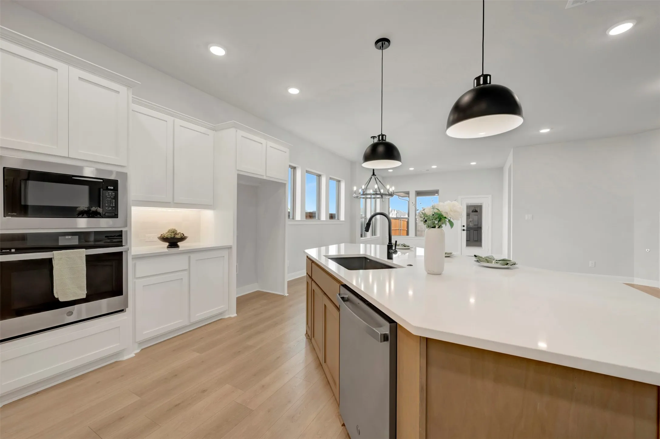 Dual tone kitchen with two tone cabinetry, stainless steel appliances, light wood finished floors, an island with sink, and light stone countertops