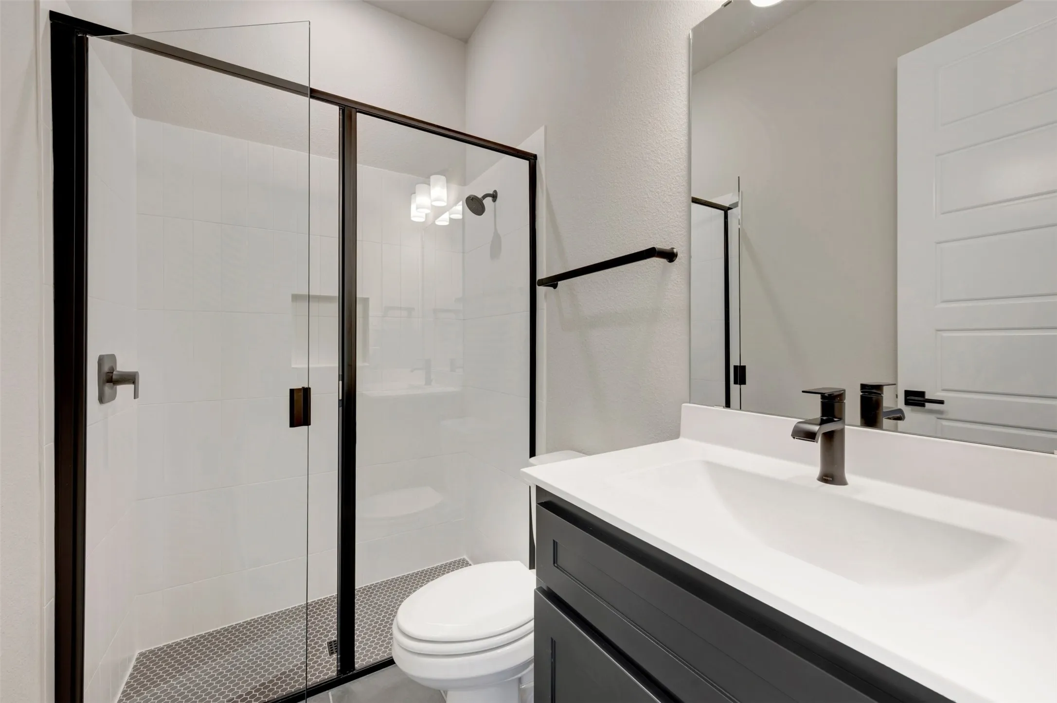 Contemporary bathroom featuring a glass-enclosed shower with matte black framing, white subway tile walls, and a hexagonal floor tile pattern