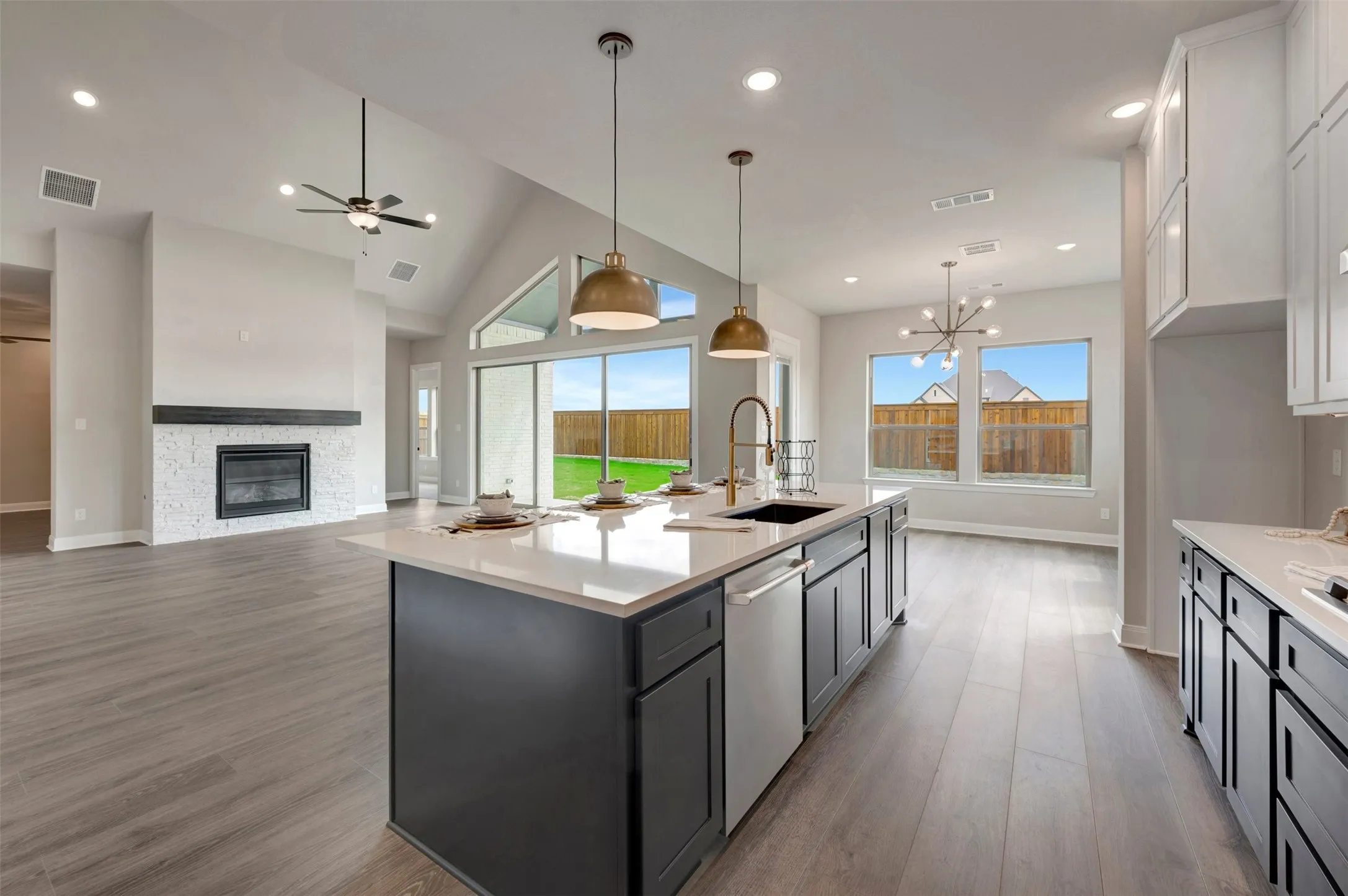 Open-concept kitchen featuring a large island with a sink and pendant lighting, white countertops, and dark cabinetry