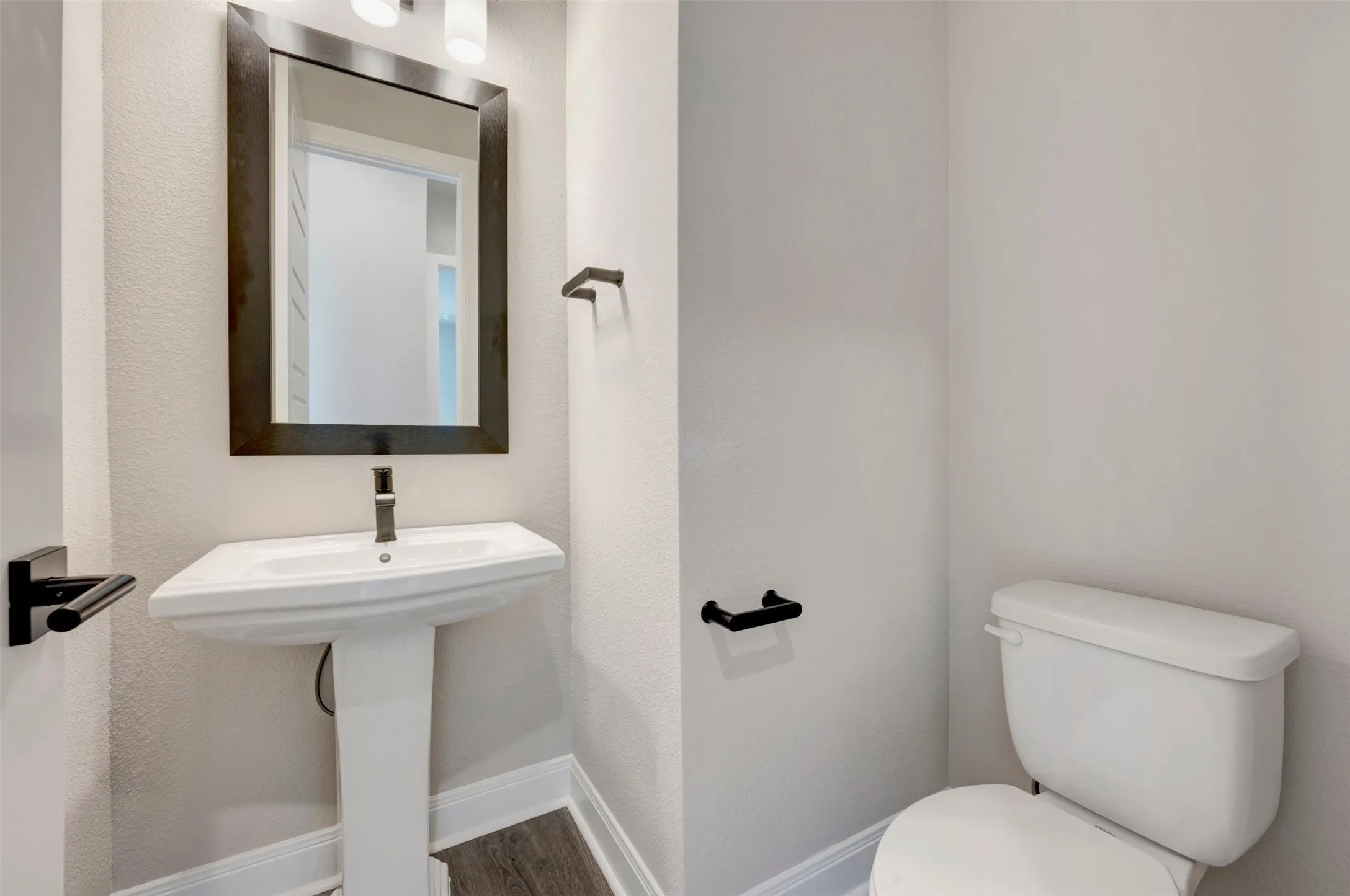 Pedestal sink with dark-framed mirror and wall-mounted light fixture