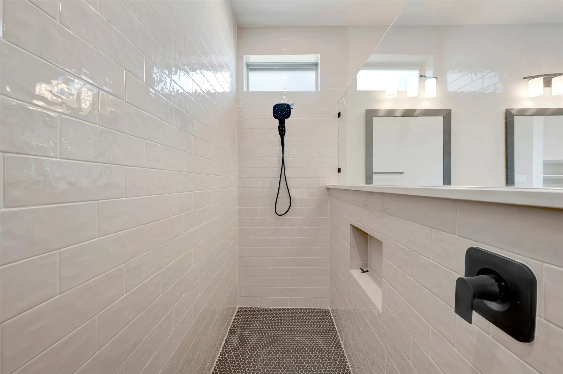 Spacious walk-in shower featuring light subway tile walls, dark hexagonal mosaic floor tiles, a built-in shower niche, and matte black fixtures