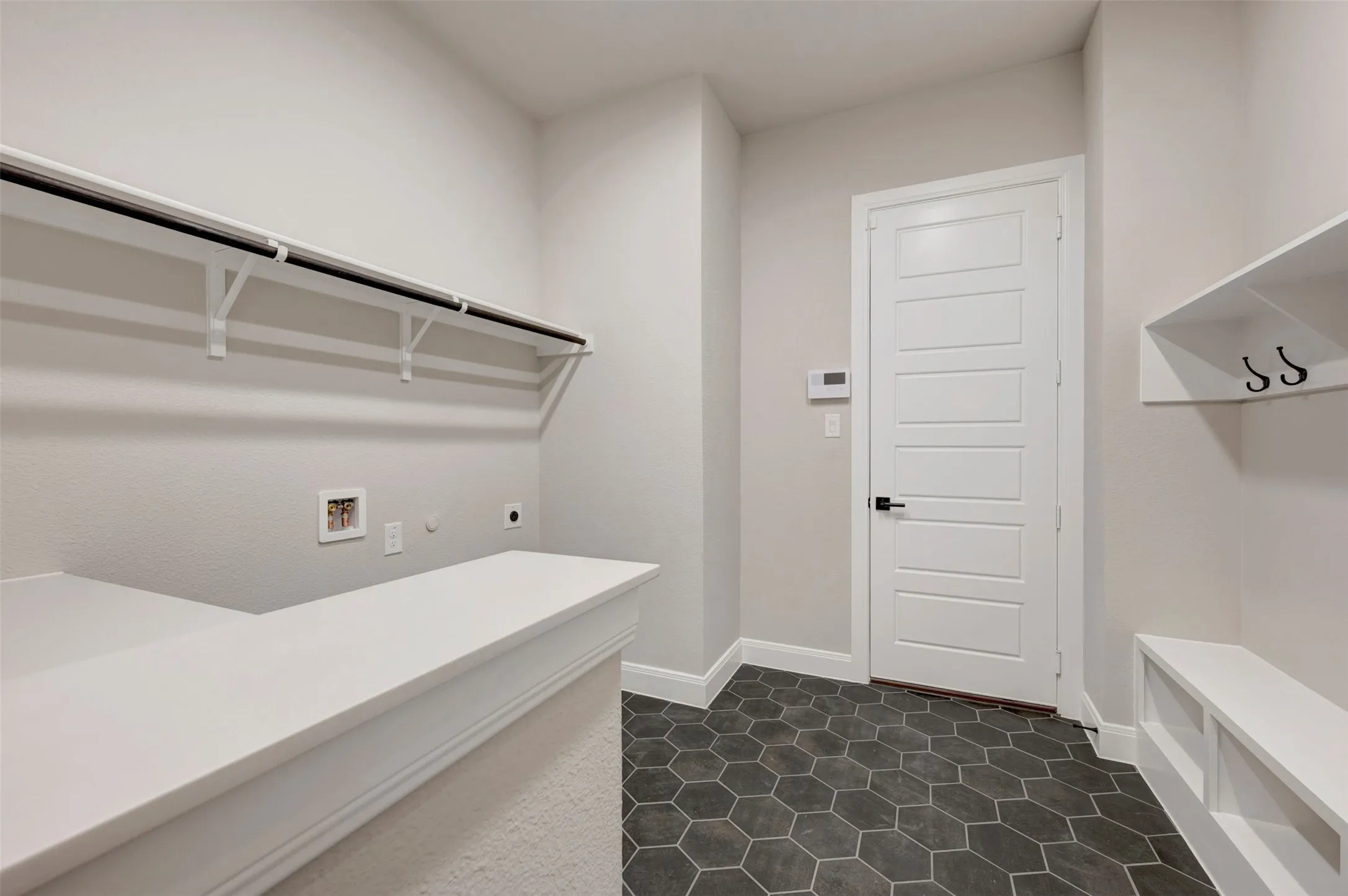 Mudroom and laundry area featuring hexagonal floor tiles, a built-in bench with storage cubbies, and a wall-mounted shelf with coat hooks