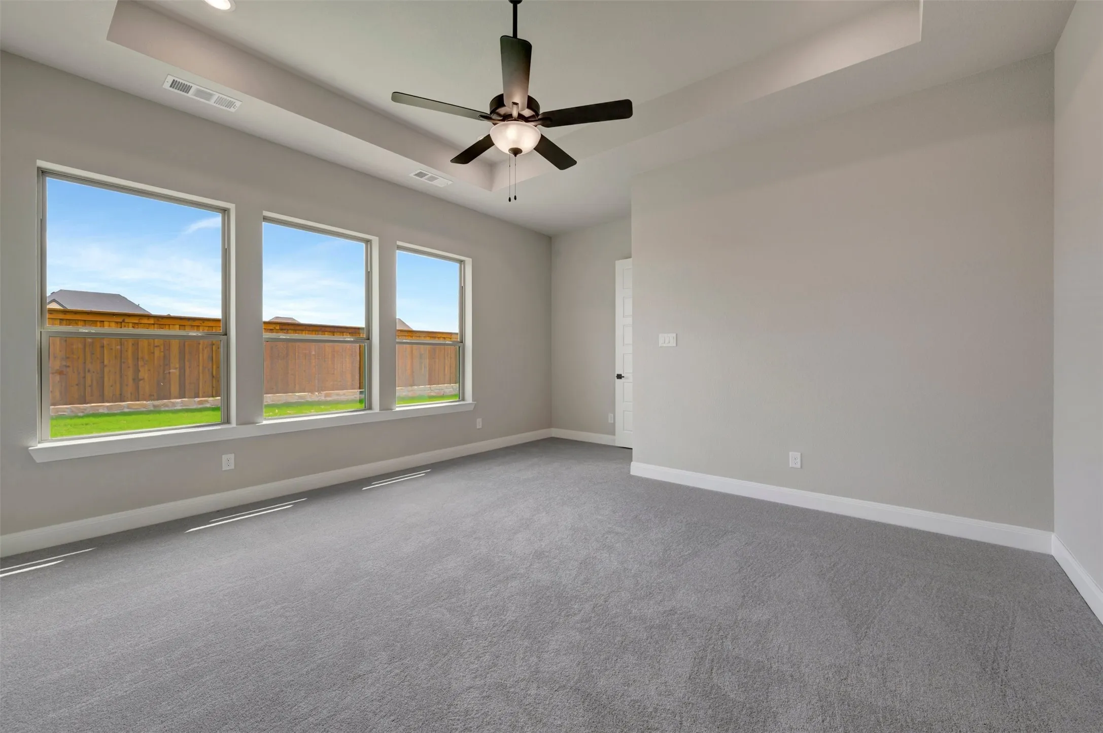 Spacious room featuring three large windows, tray ceiling with recessed lighting, and a dark-toned ceiling fan