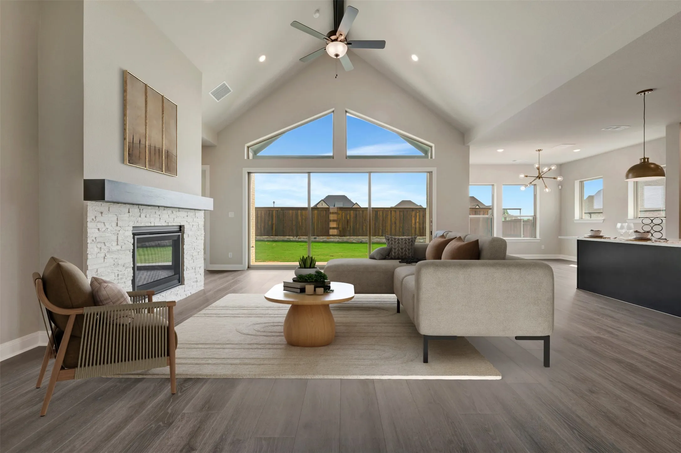 Vaulted ceiling living area featuring a stone-clad fireplace with a dark wood-finish mantel, wood-finish flooring, and expansive windows