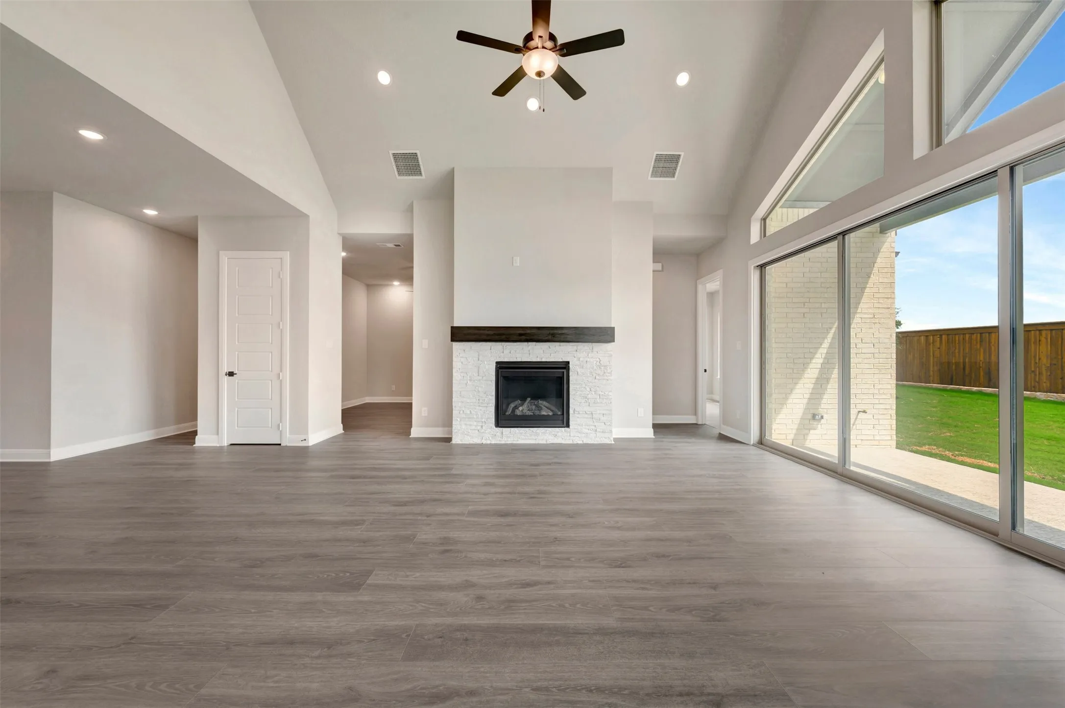 Spacious interior featuring wood-finish flooring, a contemporary fireplace with a dark wood mantel, high vaulted ceilings, and a ceiling fan
