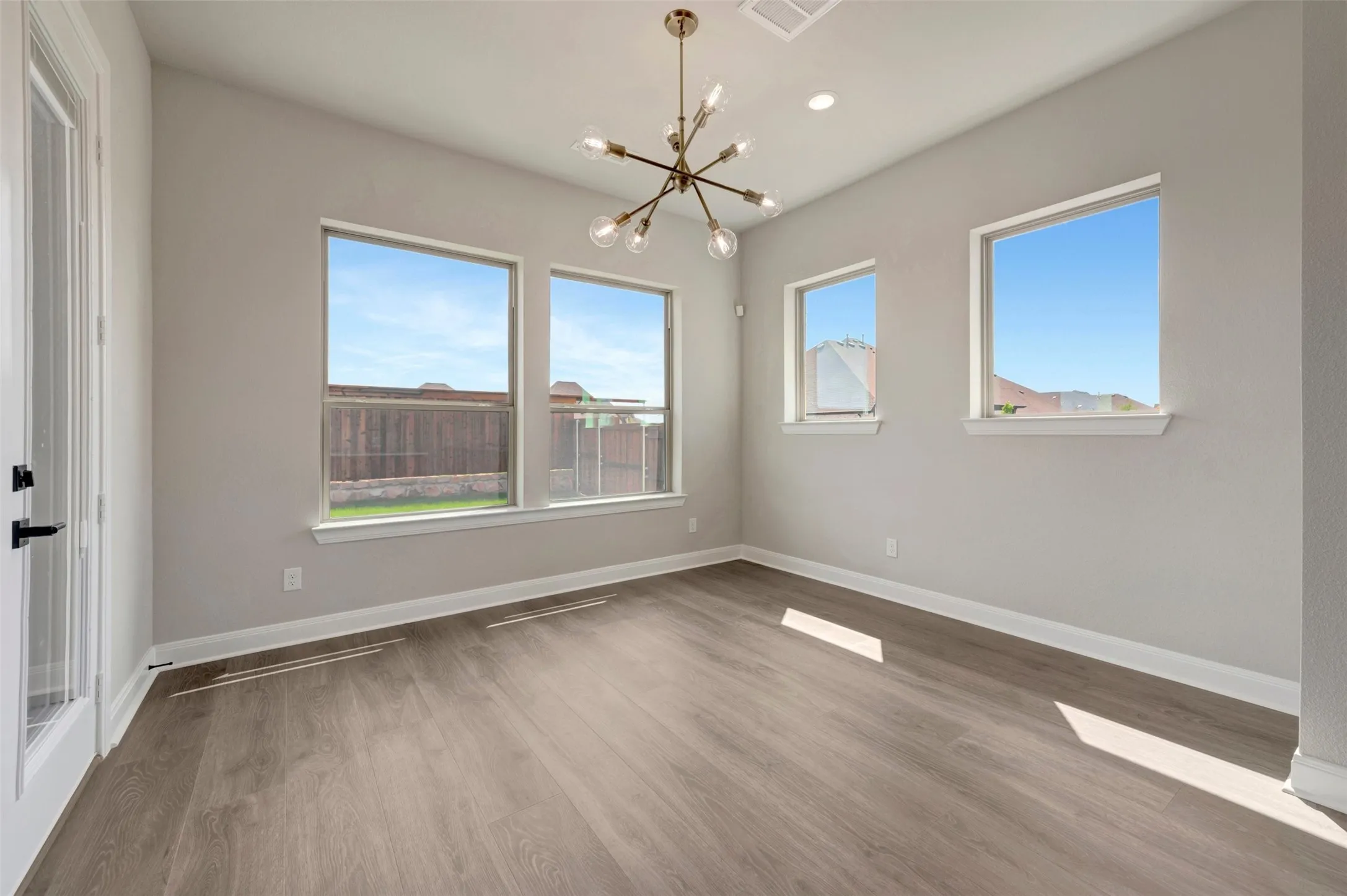 Spacious interior room featuring wood-finish flooring, light gray wall paint, and multiple windows