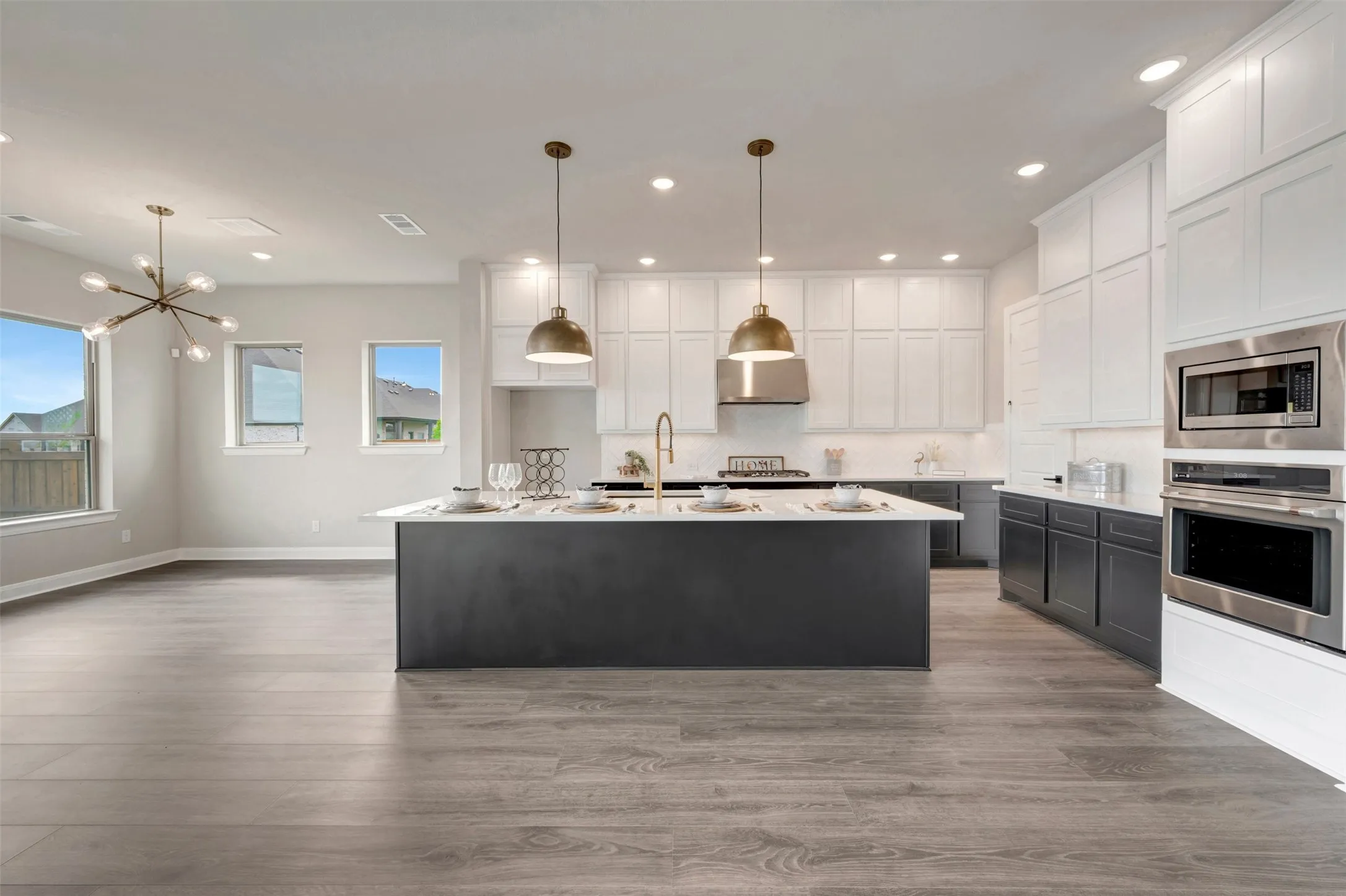Open-concept living space featuring wood-finish flooring, a kitchen island with seating, pendant lighting, stainless steel appliances, and abundant cabinetry