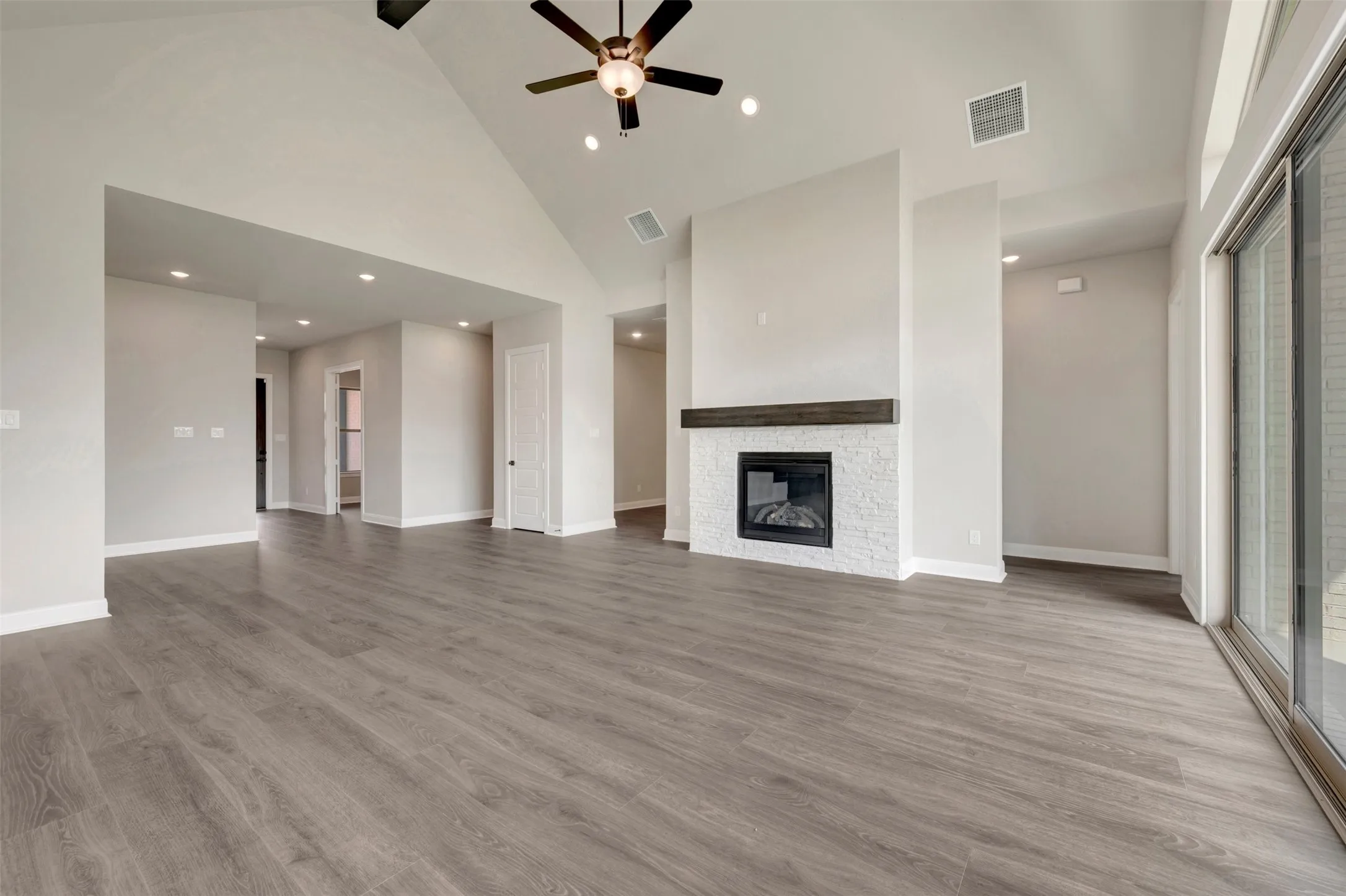 Spacious living area featuring wood-finish flooring, a vaulted ceiling, and a ceiling fan