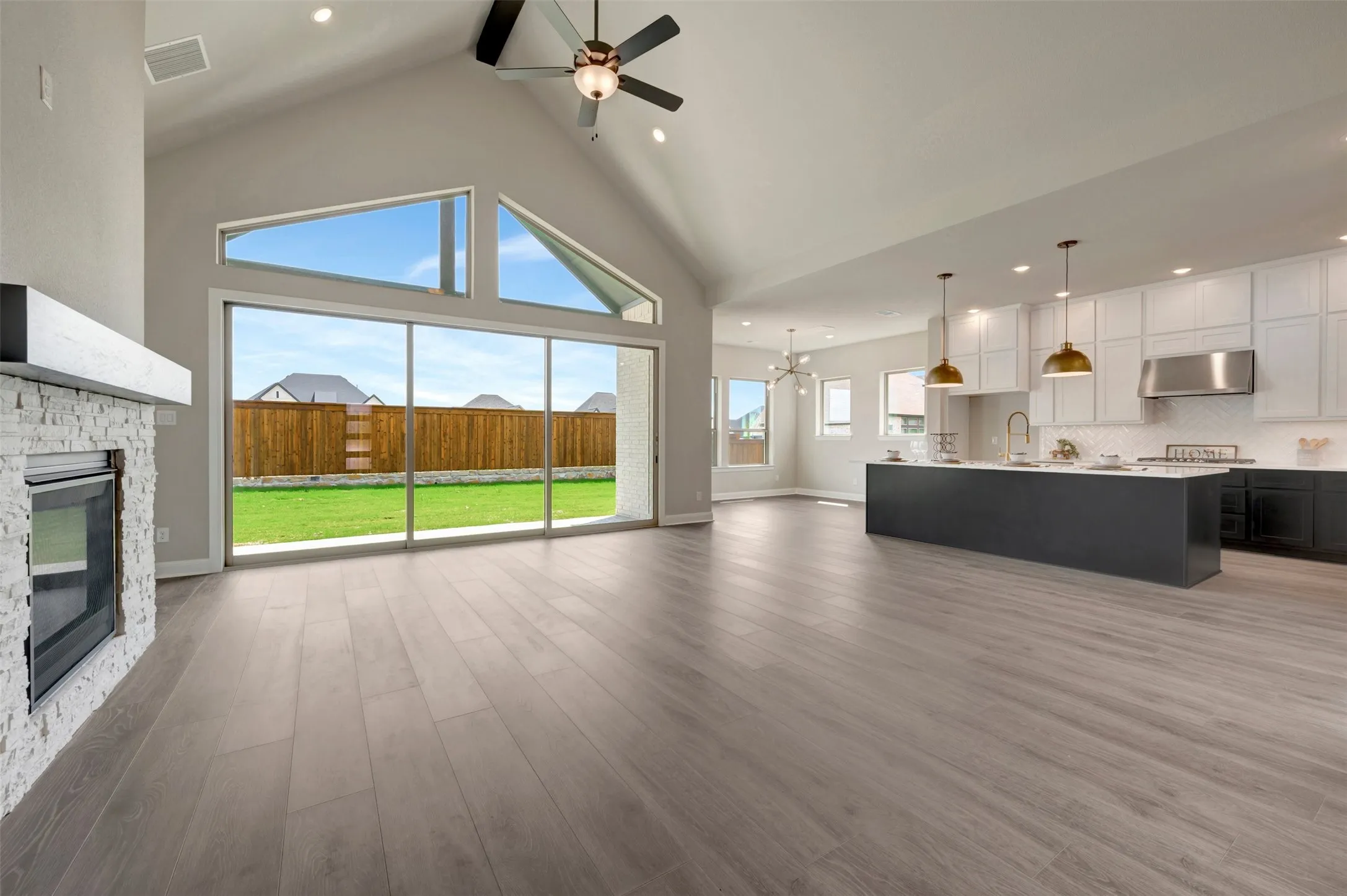 Expansive open-concept interior featuring wood-finish flooring, a vaulted ceiling, and a kitchen with an island