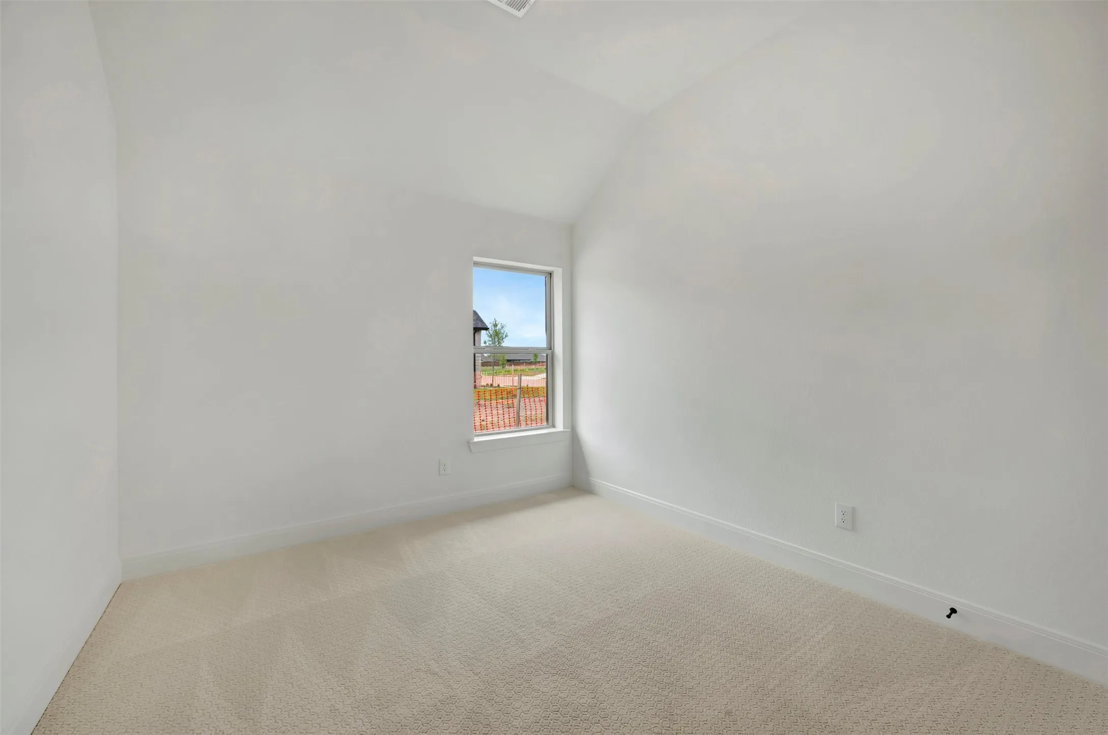 Carpeted interior room with an angled vaulted ceiling and a single window offering natural illumination