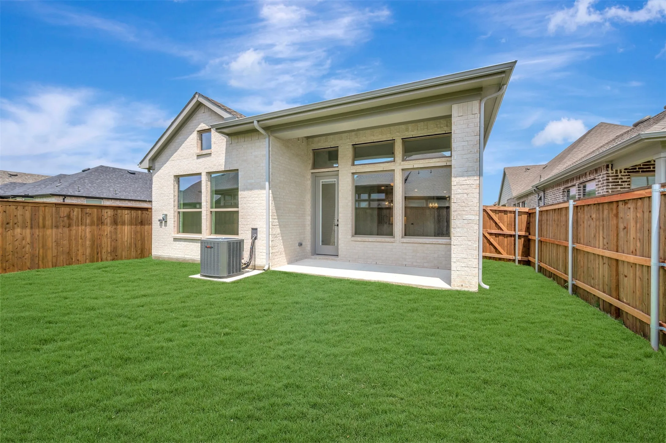 Expansive backyard featuring a manicured lawn, a covered patio, a full privacy fence, and a neutral brick exterior