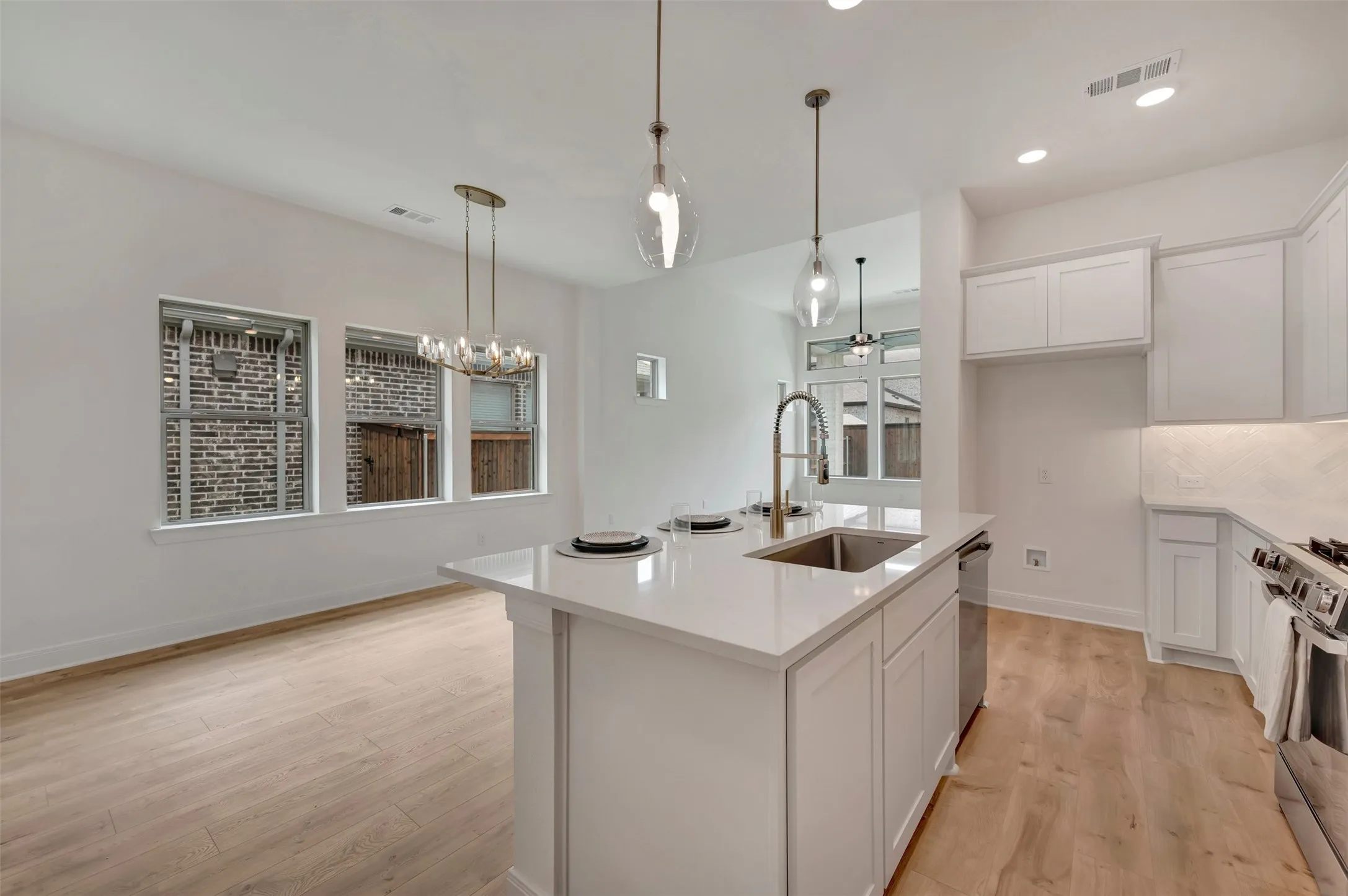 Open-concept kitchen and dining area featuring a central island with an undermount sink, quartz countertops, white cabinetry, and wood-finish flooring