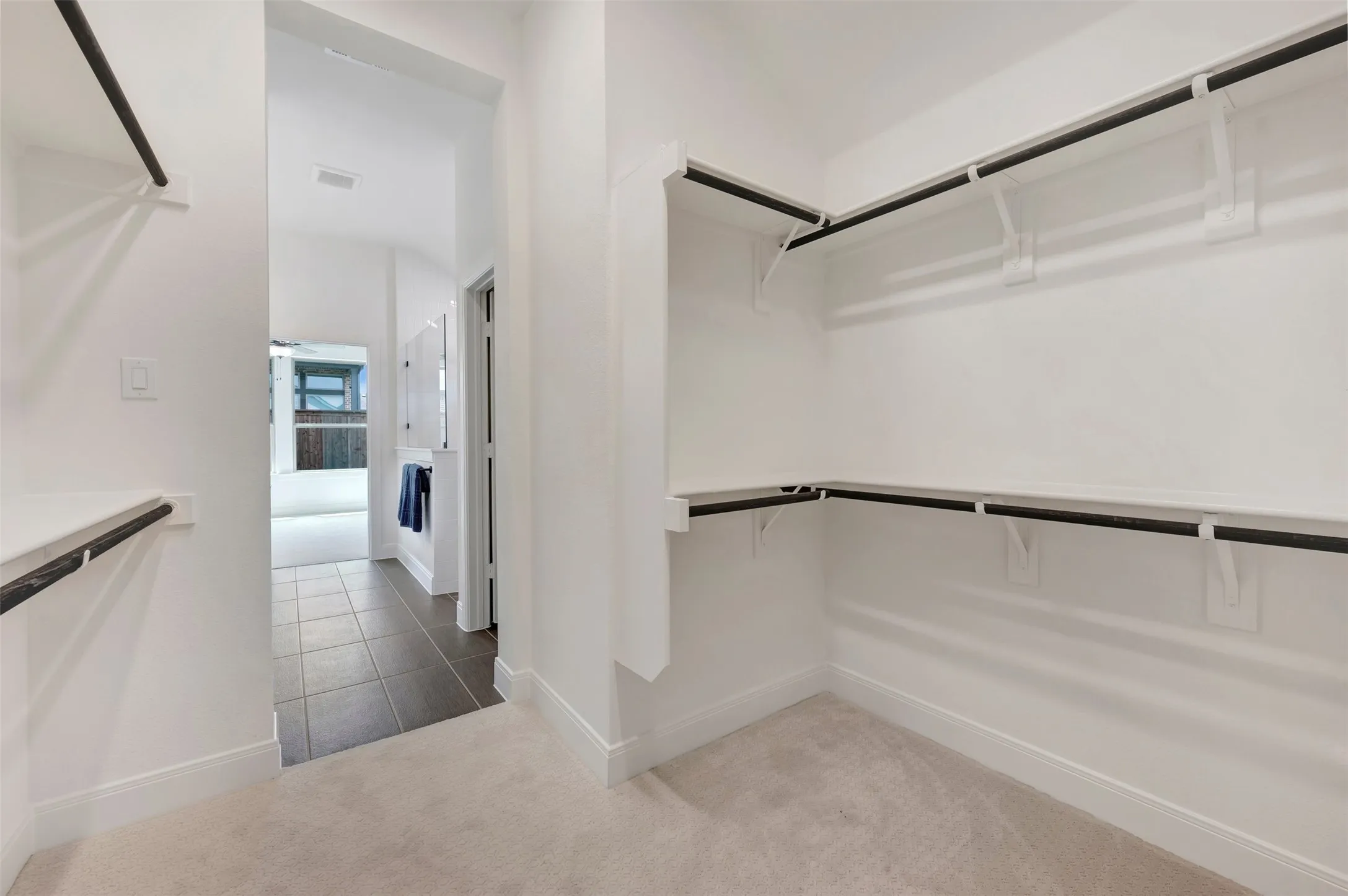 Walk-in closet featuring light-toned carpeting, white walls, and multiple levels of shelving and hanging rods