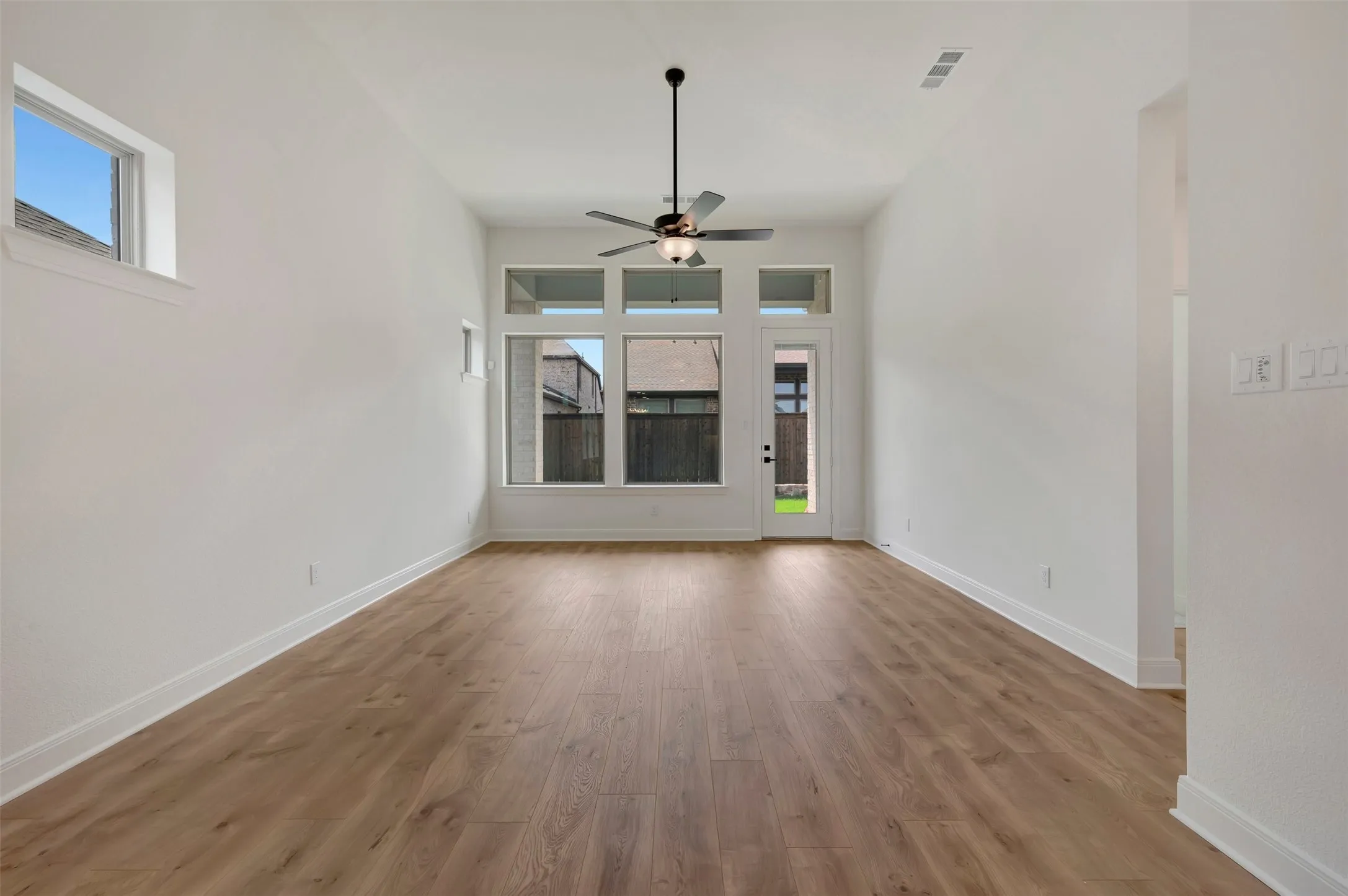 Spacious room featuring wood-finish flooring, high ceilings, and abundant natural light from multiple windows and a glass-paneled door