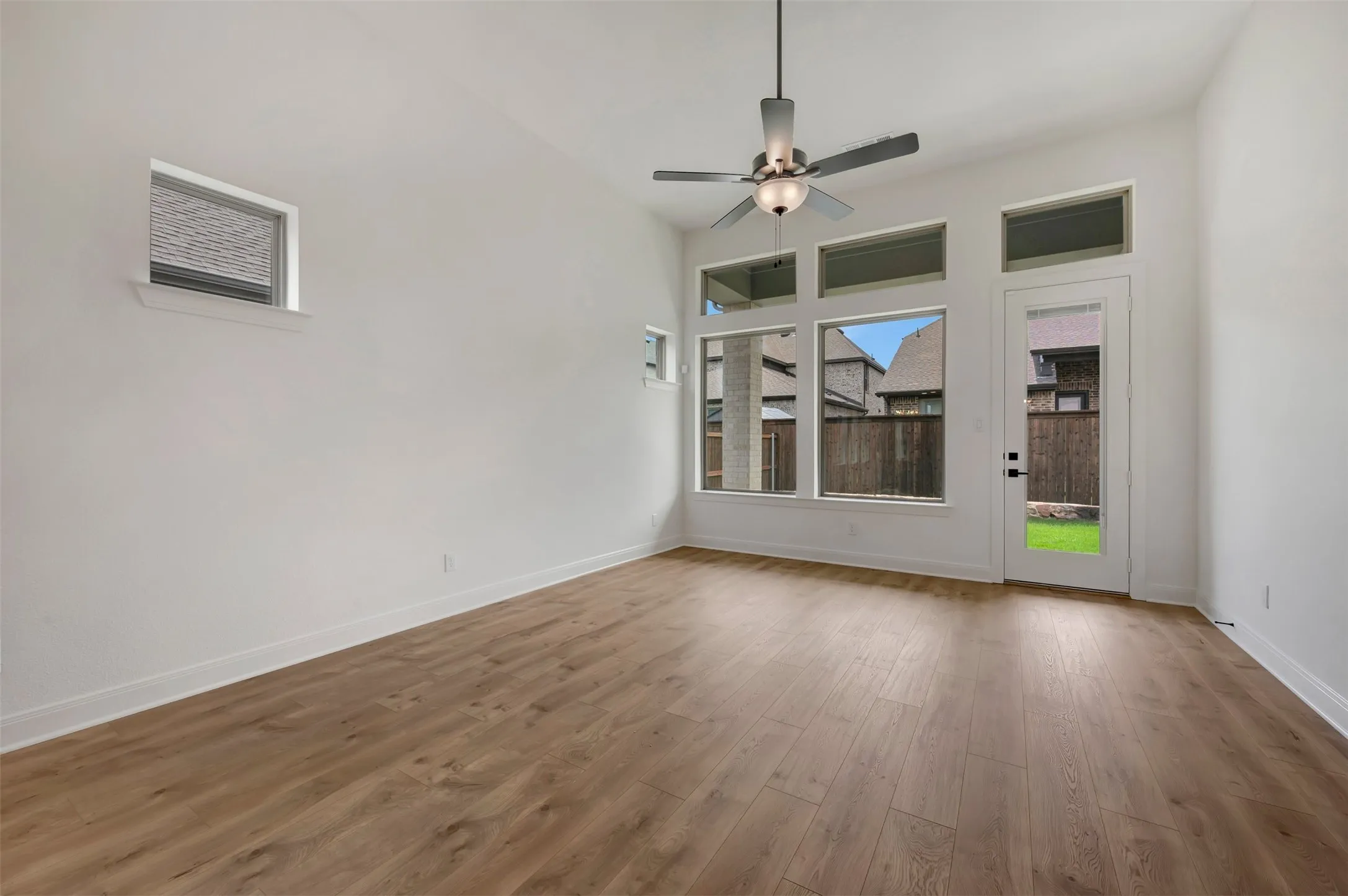 Spacious room featuring wood-finish flooring, high ceilings, and a modern ceiling fan with integrated lighting