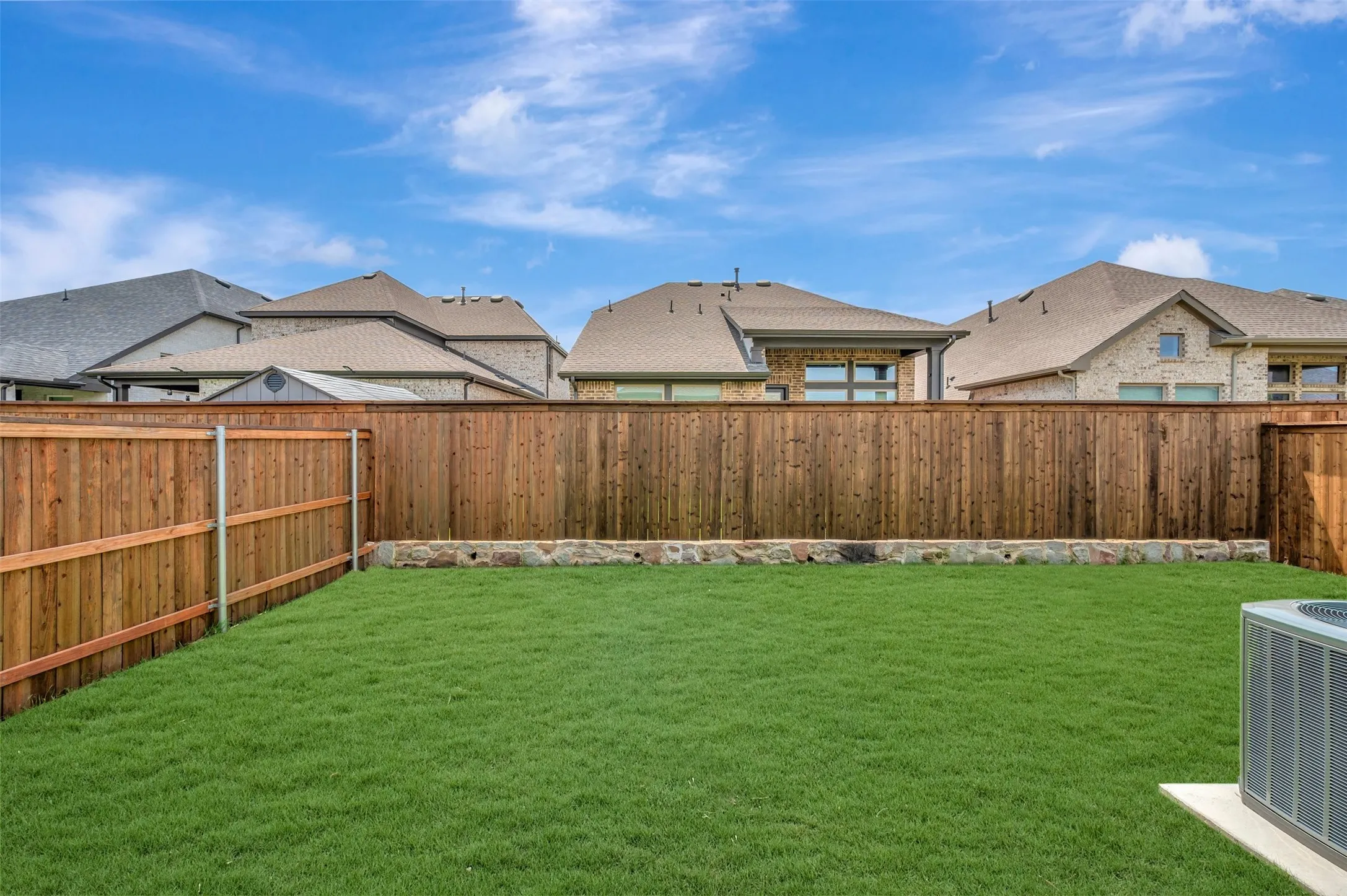 Expansive backyard featuring a lush lawn, wood privacy fencing, and a stone-faced retaining wall