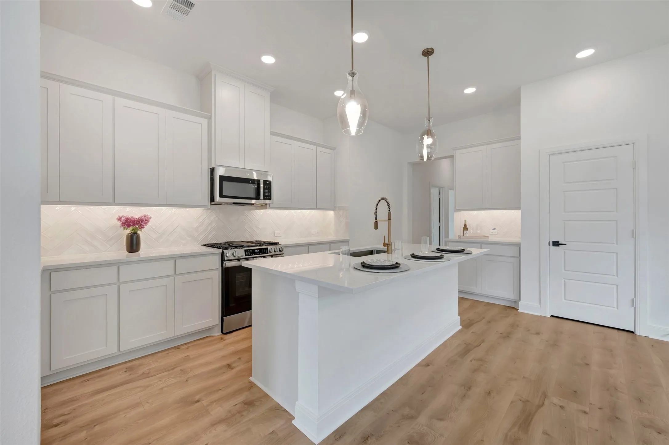 Open-concept kitchen featuring an island with seating, pendant lighting, white shaker cabinetry, stainless steel appliances, and wood-finish flooring
