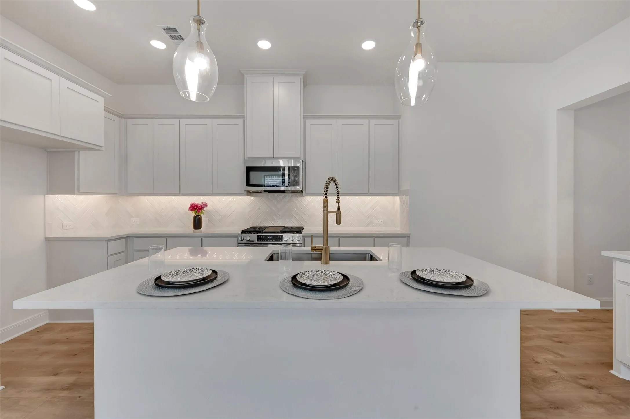 Bright kitchen featuring a large central island with a sink, white cabinetry, integrated stainless steel appliances, and wood-finish flooring