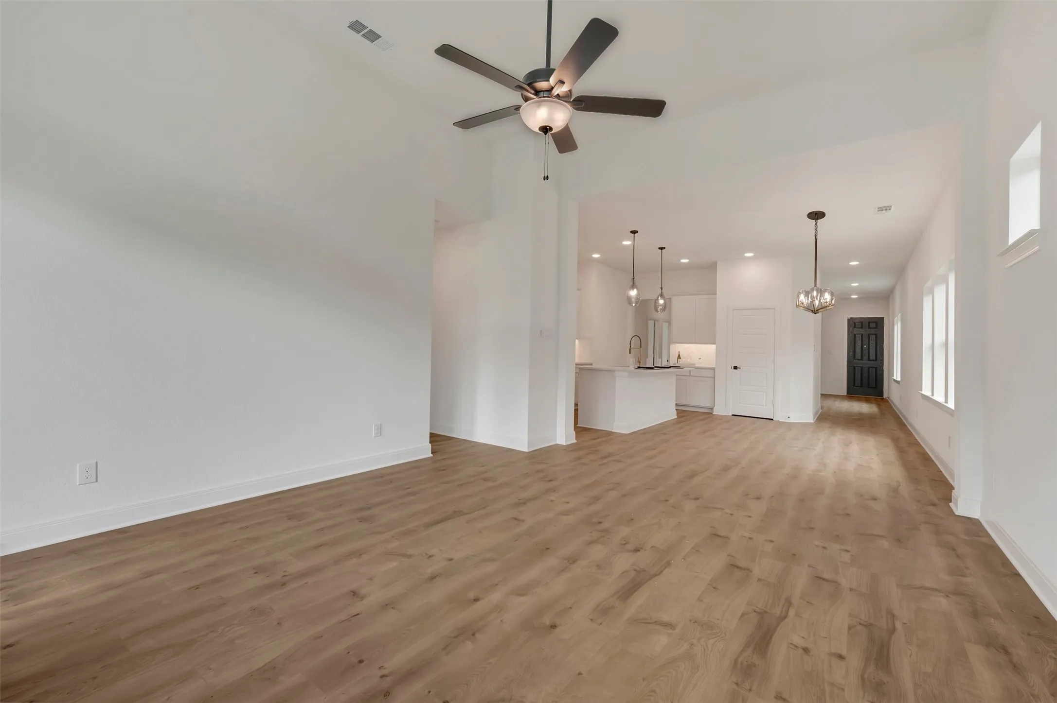Open-concept living space featuring wood-finish flooring, a vaulted ceiling, and a ceiling fan with integrated lighting