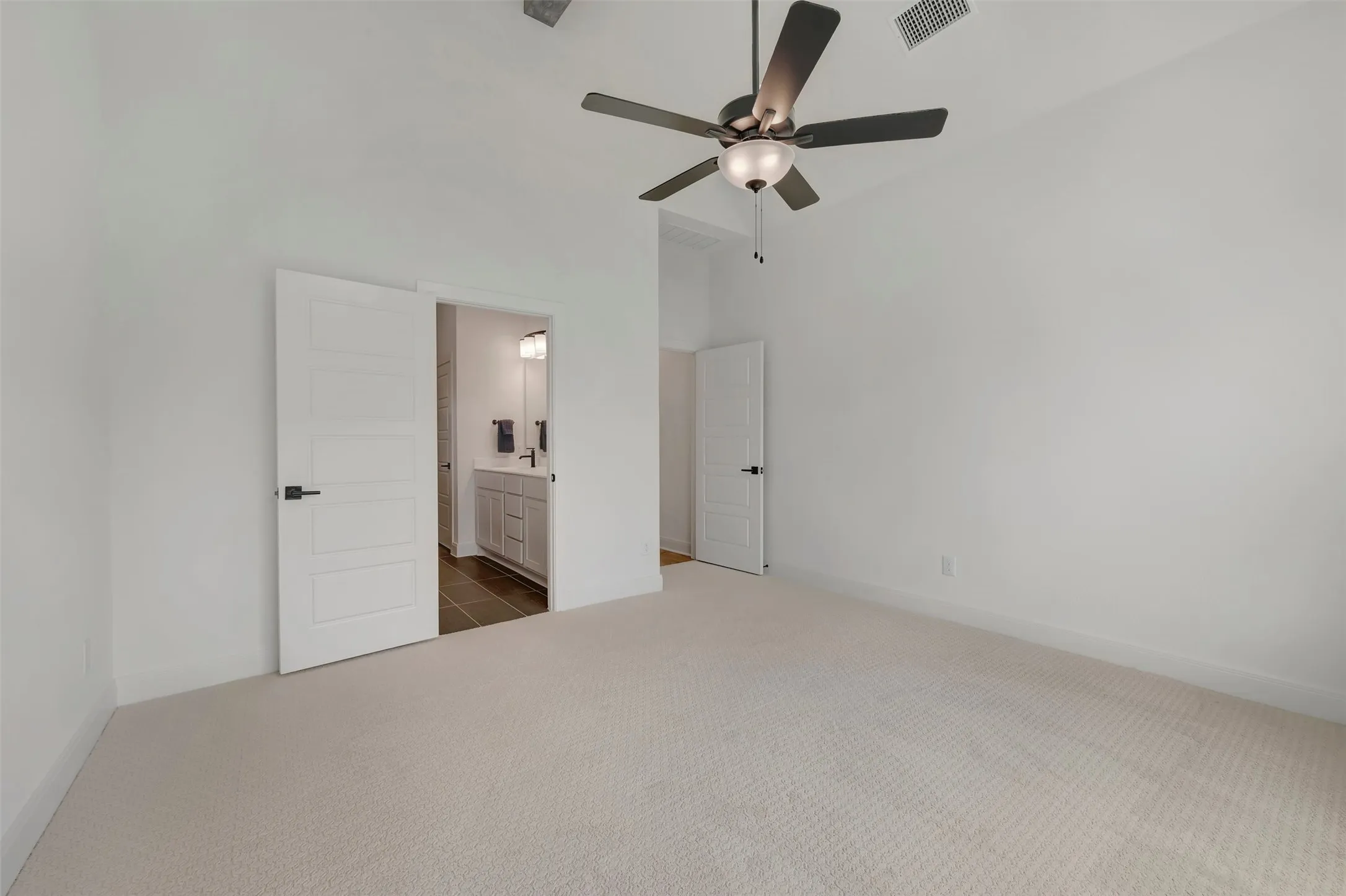 Spacious room featuring light-colored carpeting, a ceiling fan with integrated lighting, and a white interior door with black hardware