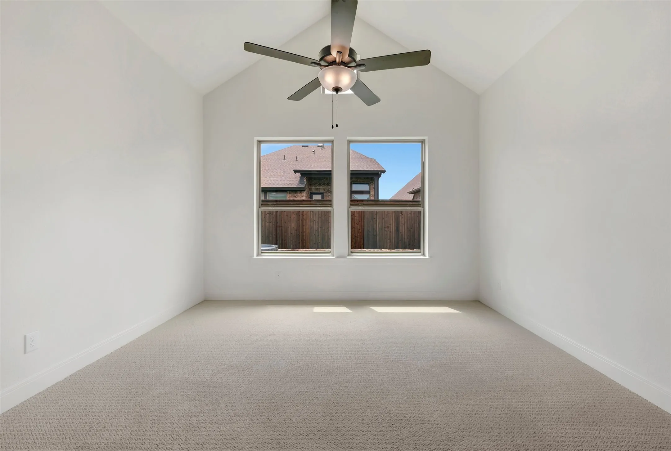 Vaulted ceiling room featuring two windows, neutral tone carpeting, and a ceiling fan with integrated lighting