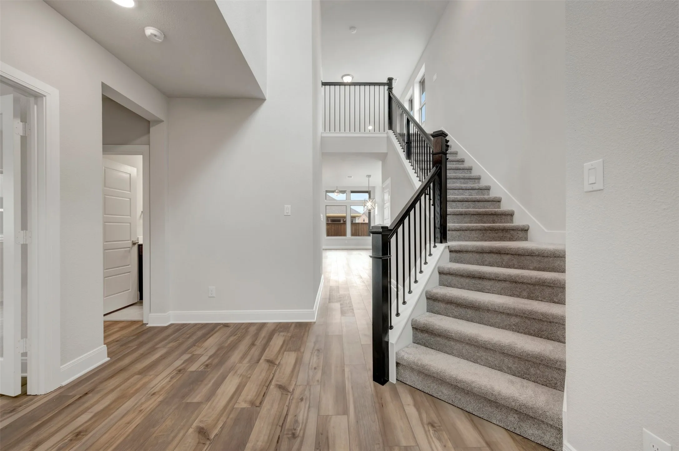 Two-story entry foyer featuring wood-finish flooring, a carpeted staircase with dark wood newel posts, and wrought iron balusters