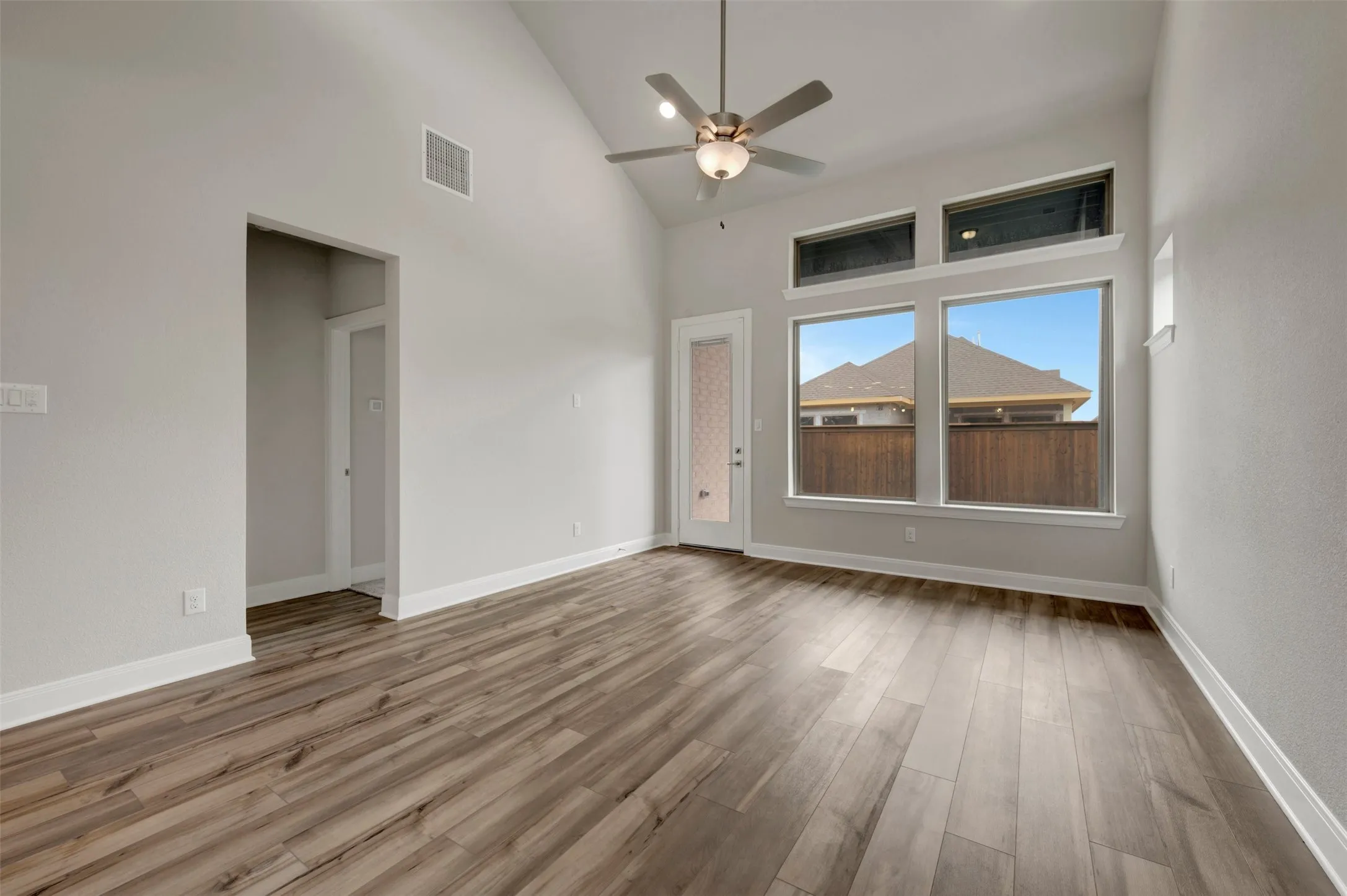Spacious interior featuring a vaulted ceiling with a ceiling fan, wood-finish flooring, multiple windows, and a glass-paneled door