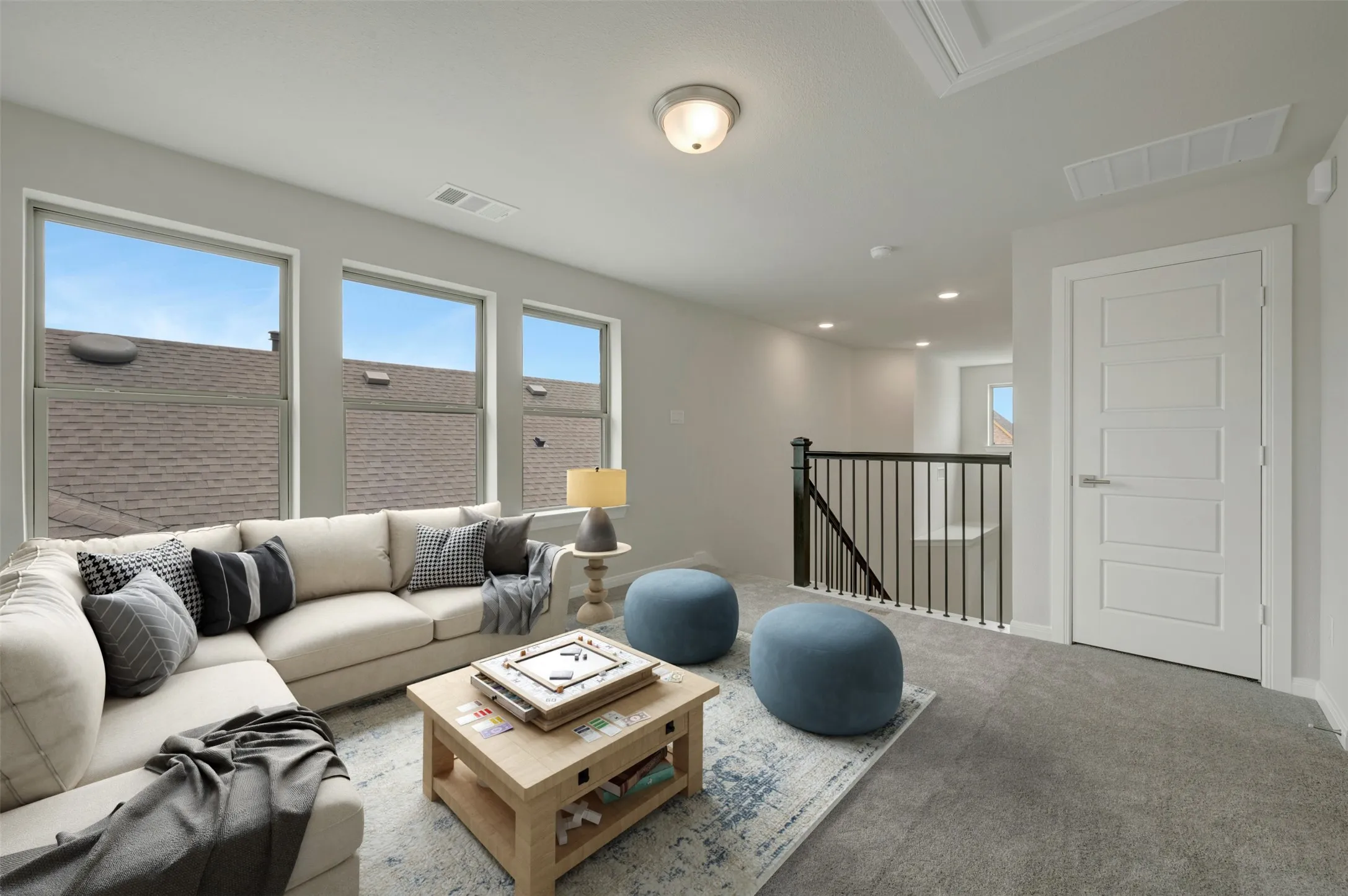 Carpeted bonus room featuring multiple windows, white paneled door, black metal railing, and a ceiling-mounted light fixture